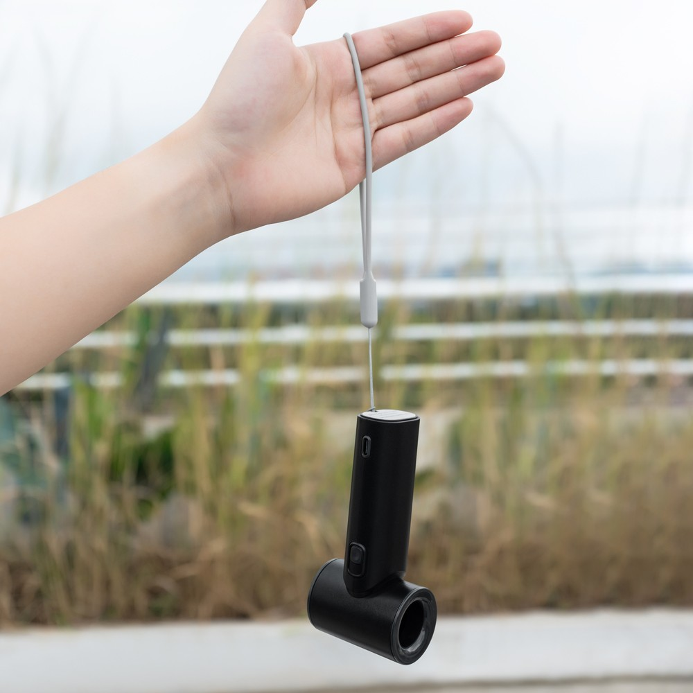 Una mano sostiene un dispositivo negro con cordón. Al aire libre en un día nublado.