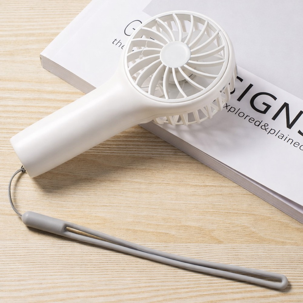 Un ventilador blanco de mano con correa gris descansa sobre un libro.