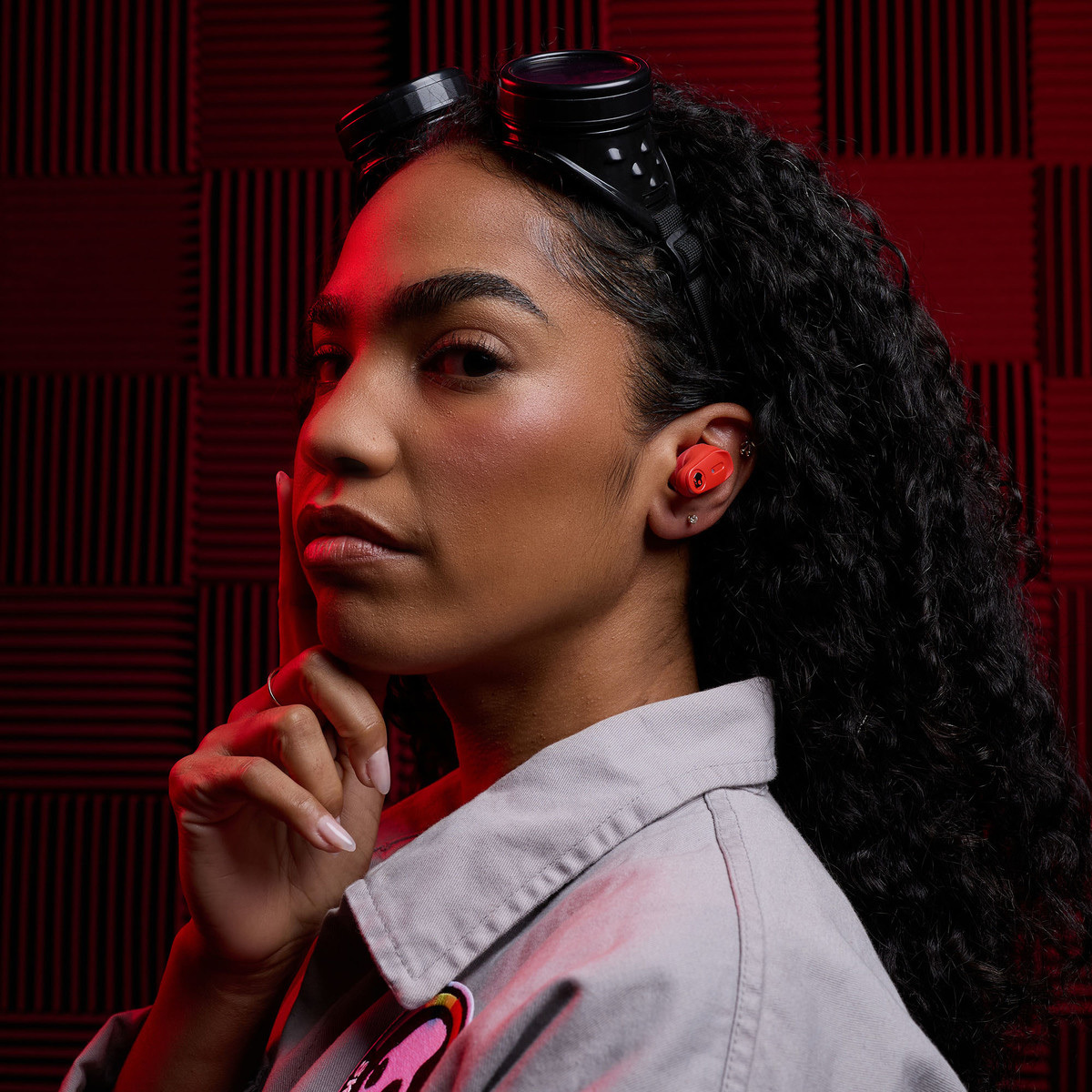 Kobieta z czerwonymi słuchawkami i goglami na głowie na tle teksturowanym.