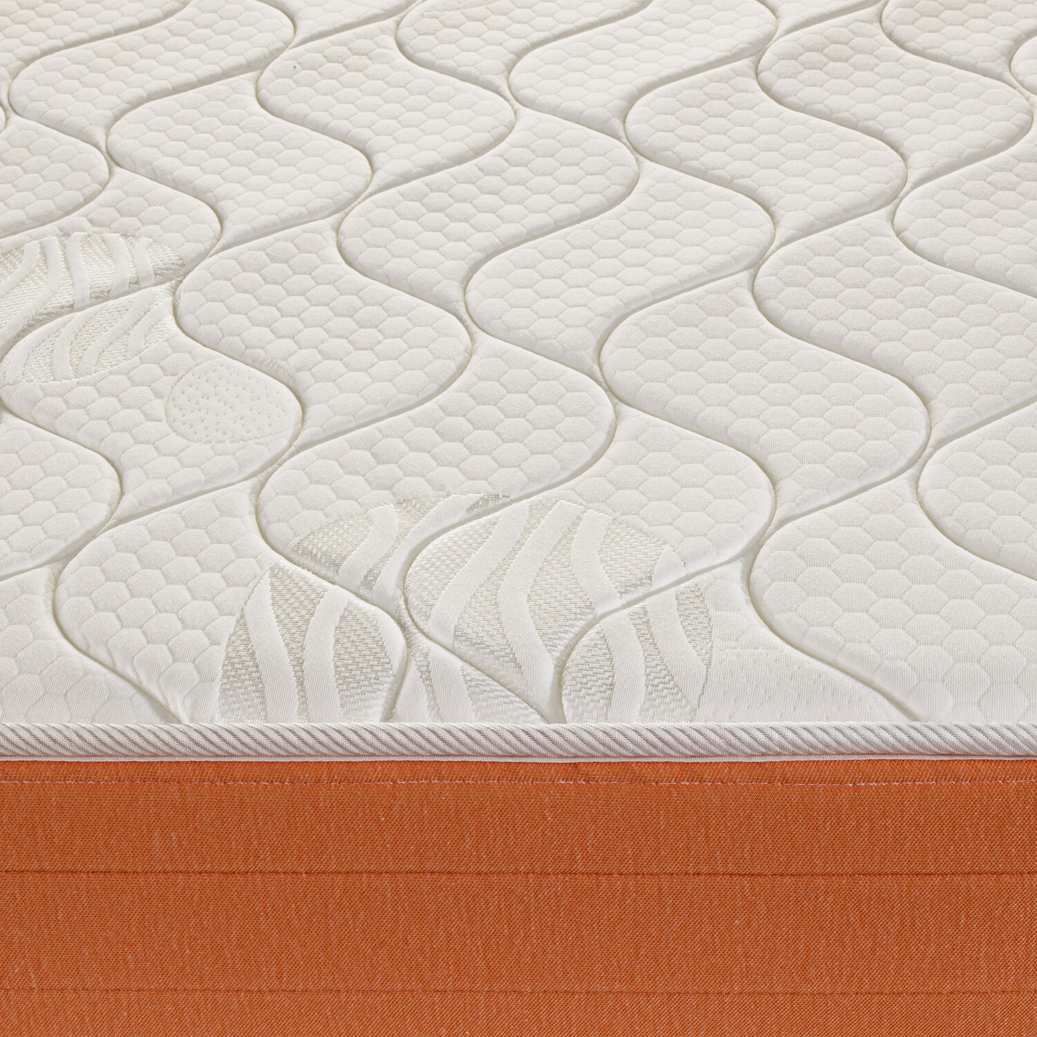 Primer plano de un colchón con parte superior acolchada blanca y base de tela naranja.