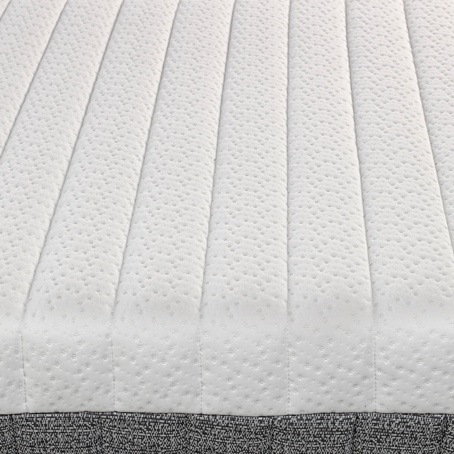 Primer plano de un colchón blanco con líneas acolchadas y textura punteada.