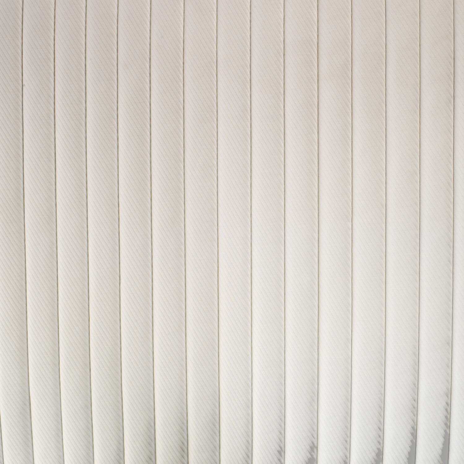 Primer plano de una superficie beige claro, acolchada verticalmente con pliegues paralelos y costuras finas.