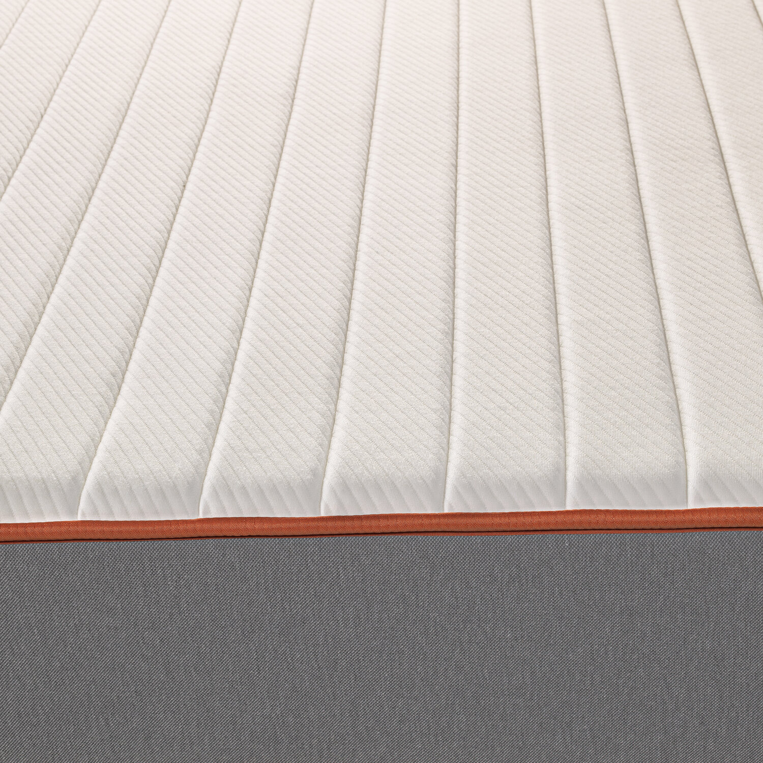 Un colchón blanco acolchado con borde naranja y lateral gris.