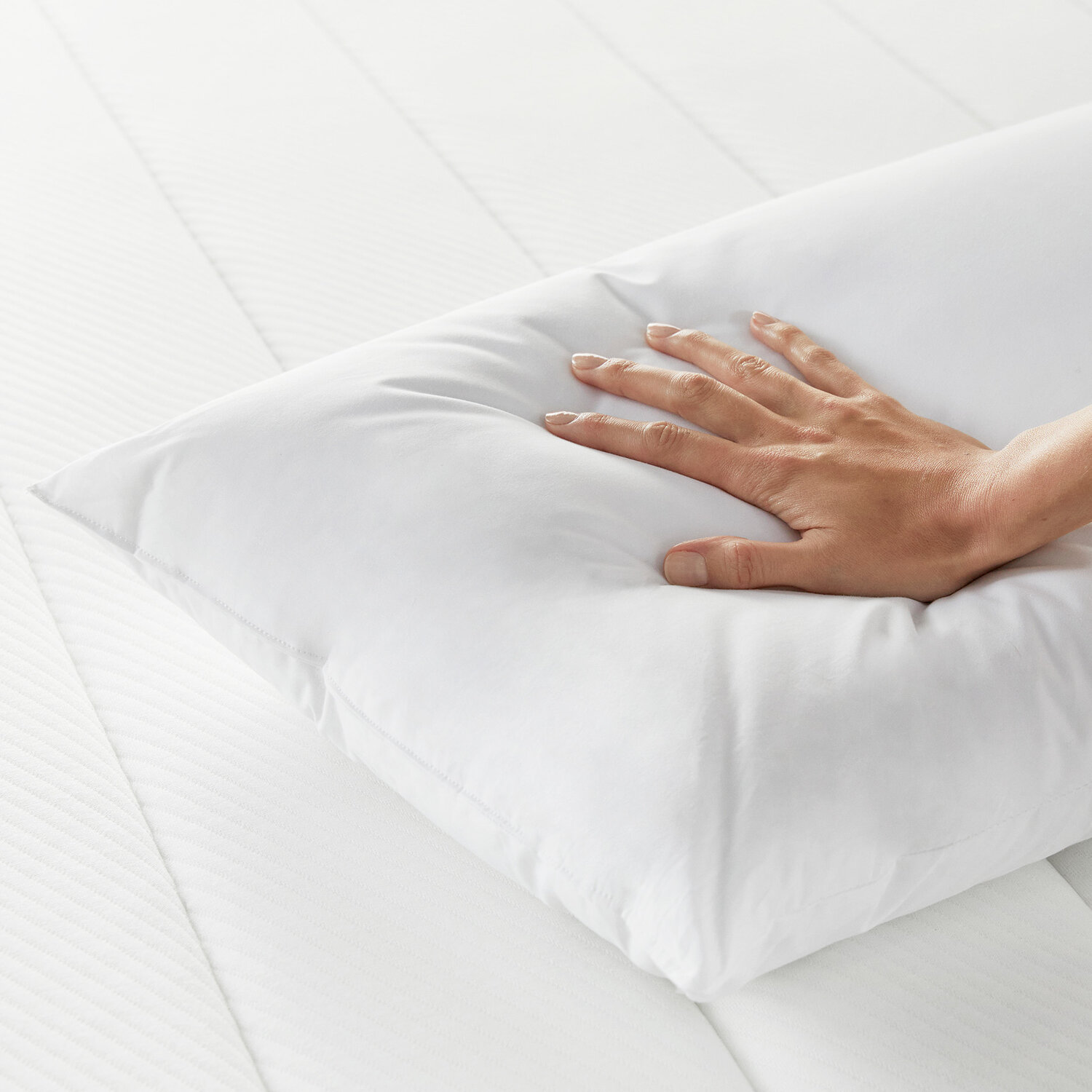 Una mano presiona una almohada blanca y suave sobre un colchón blanco a rayas.