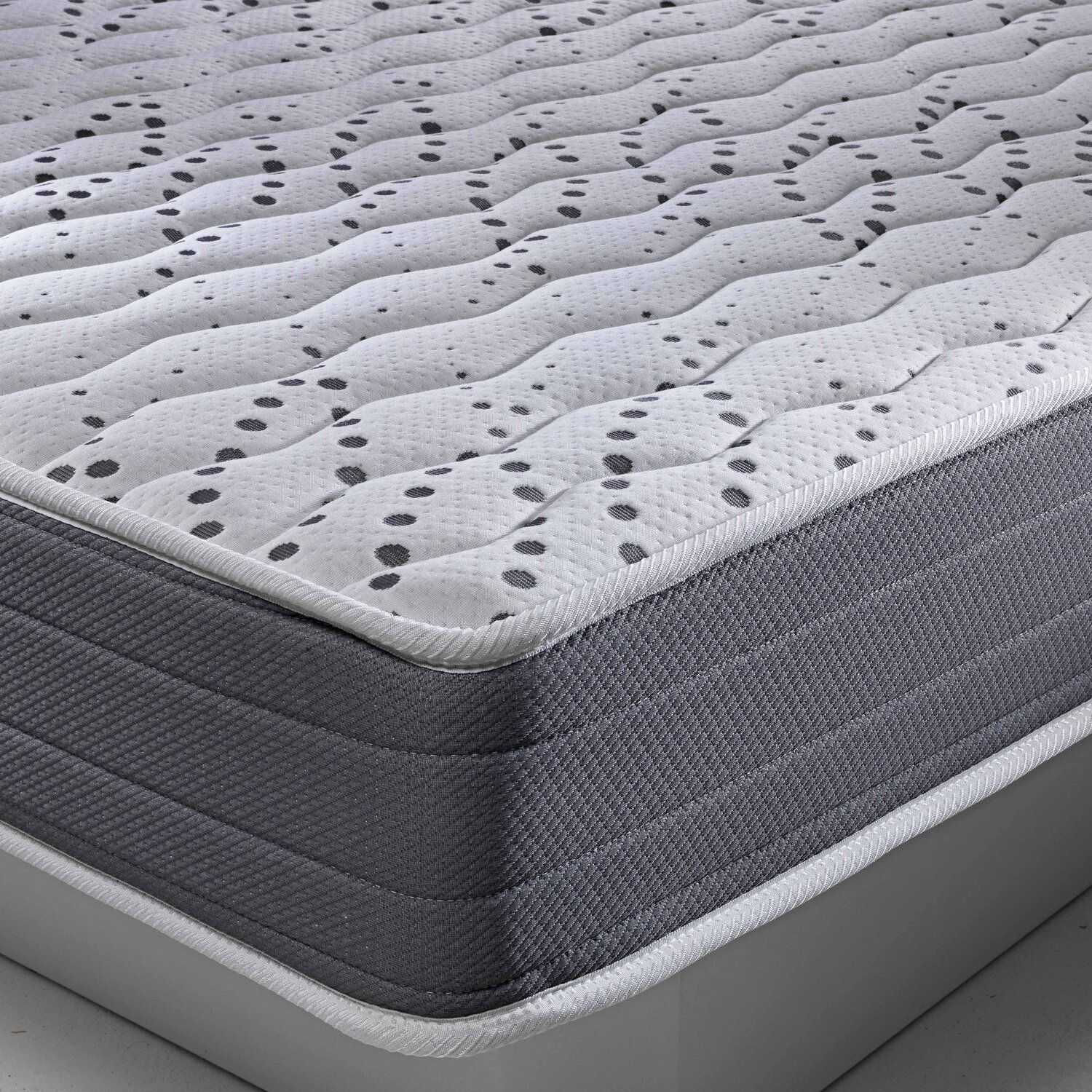 Primer plano de un colchón blanco con puntos grises y borde lateral gris.
