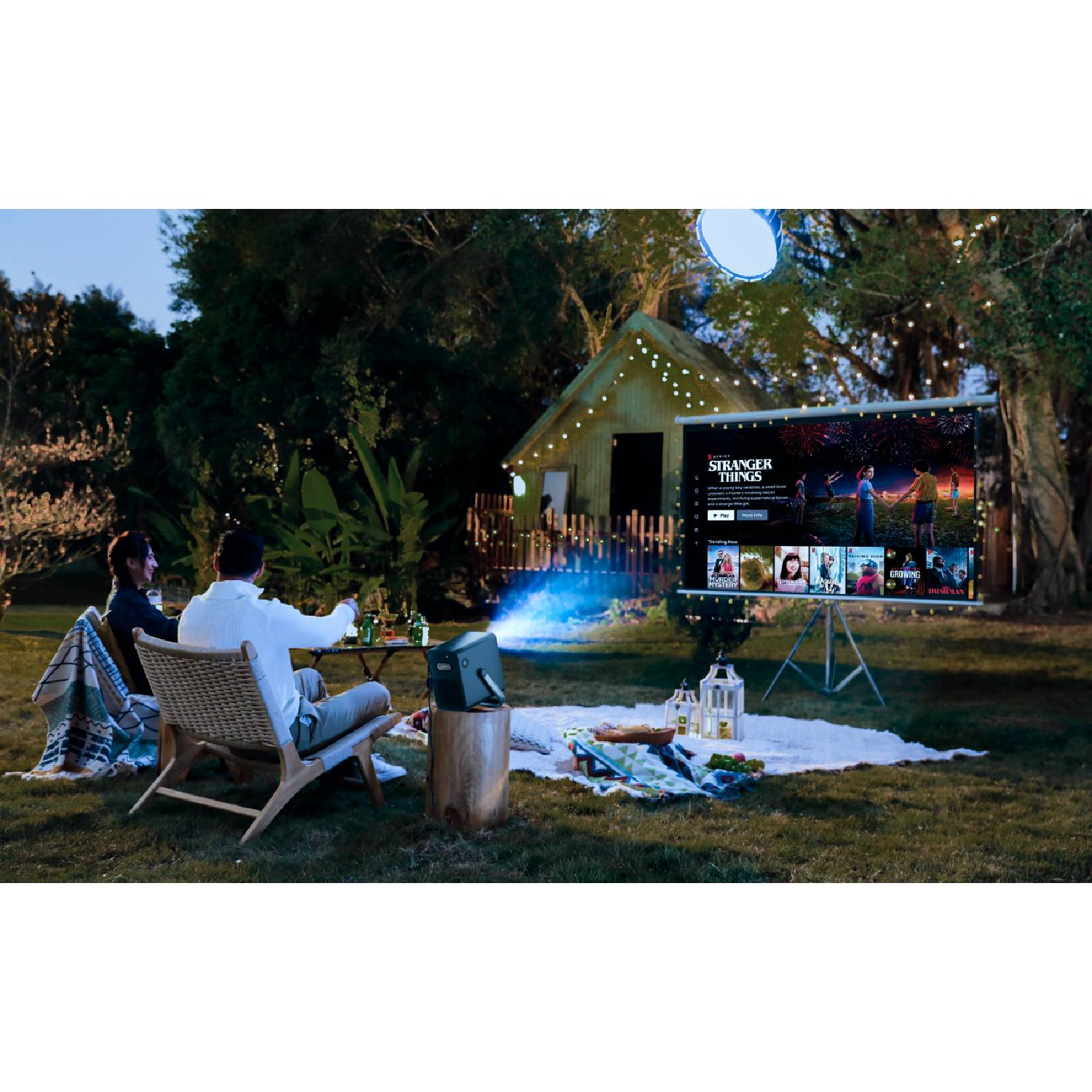Paar schaut Film im Freien auf Leinwand, Projektor wirft Licht auf sie.