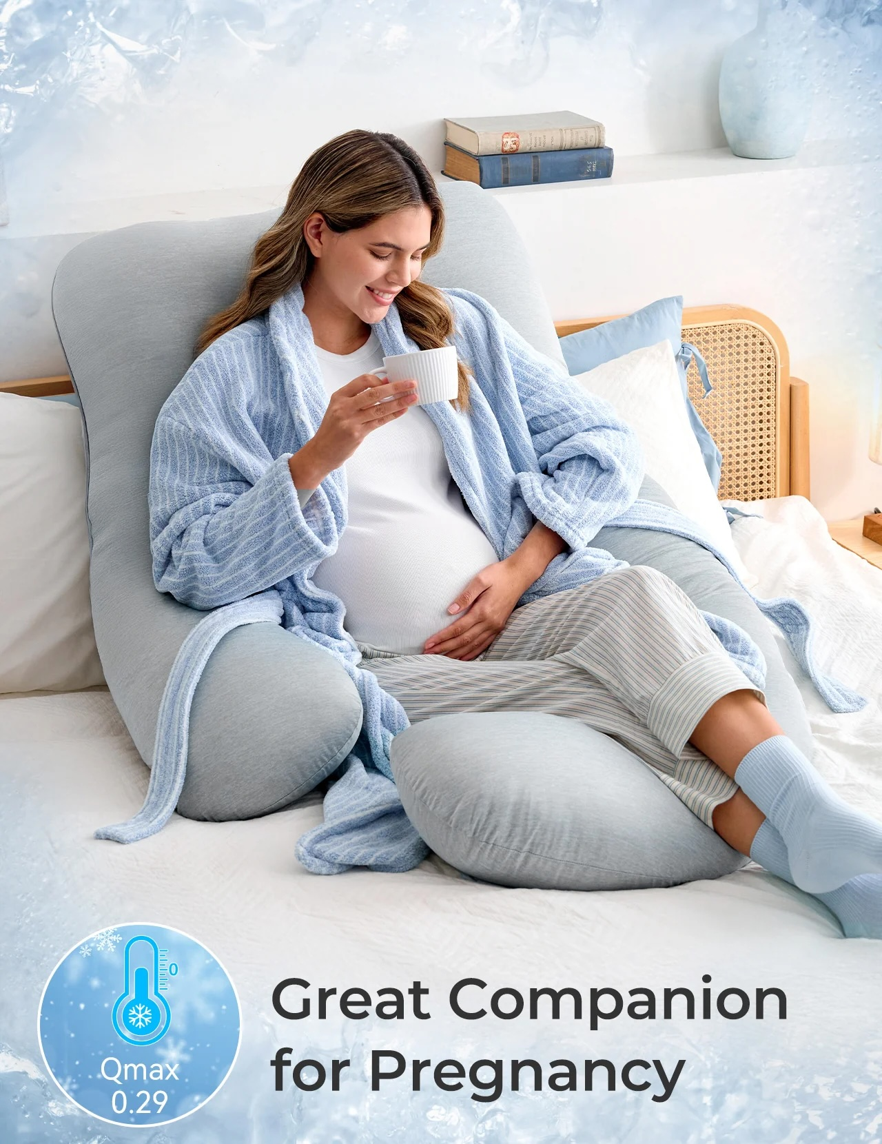 Femme enceinte en robe bleue boit dans une tasse, soutenue par un oreiller gris.