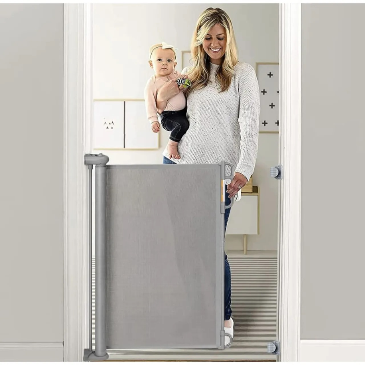 Eine Frau hält ein Baby, während sie eine graue Absperrung in einer Tür hält.