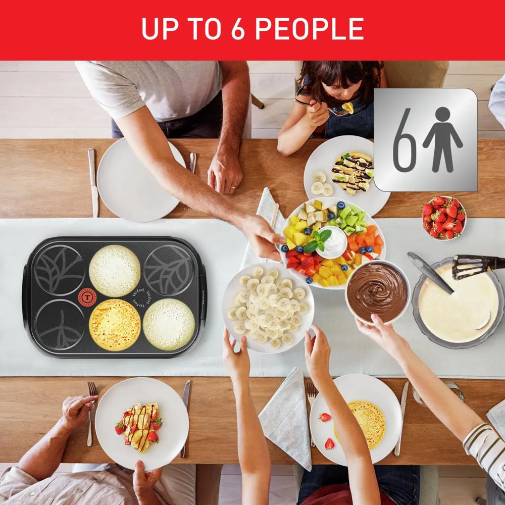 Sześć osób je naleśniki z owocami i czekoladą przy stole.