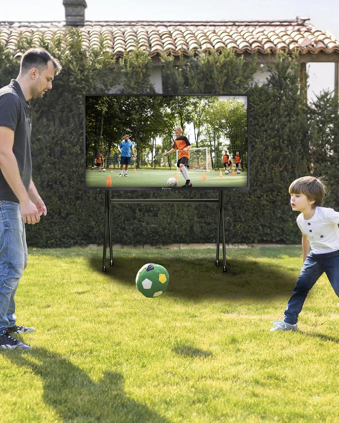 Mann und Junge spielen Fußball im Garten vor einem Bildschirm.