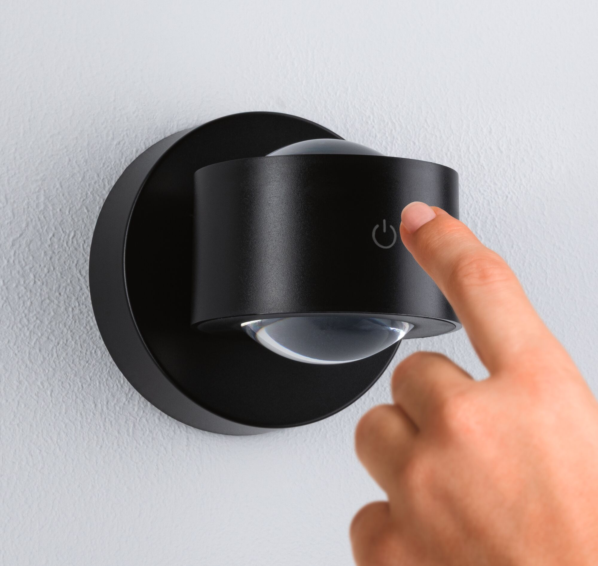 Dłoń naciska przycisk zasilania na czarnej lampie ściennej.