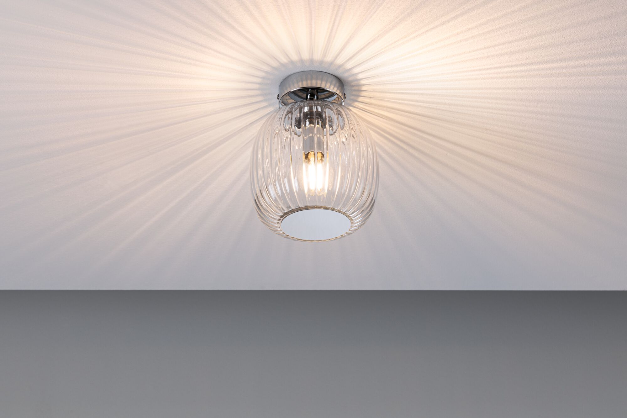 Eine Deckenleuchte mit einem durchsichtigen Glasdiffusor, der Strahlen an die Decke wirft.