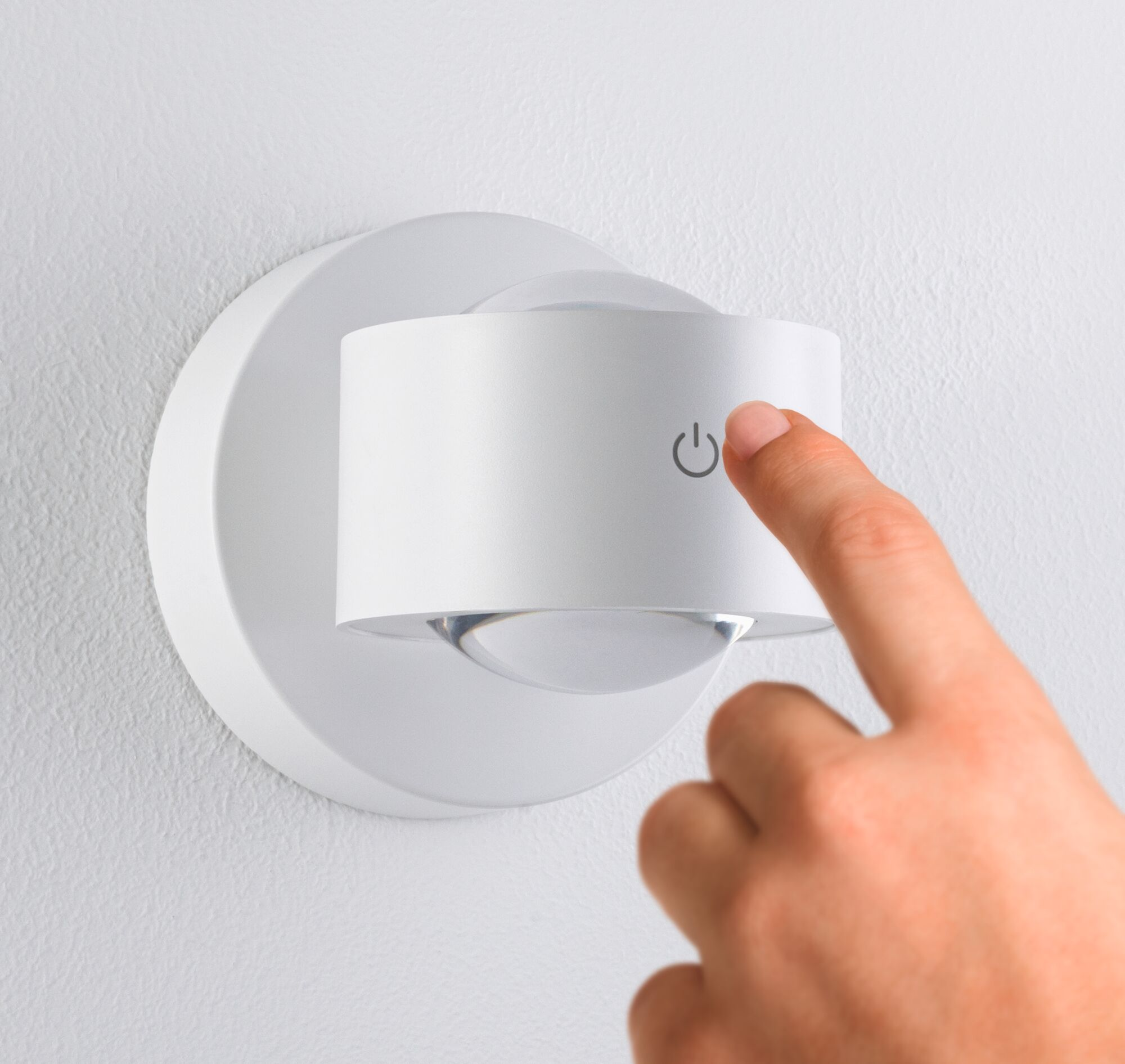 Palec naciska ikonę zasilania na białej lampie ściennej.