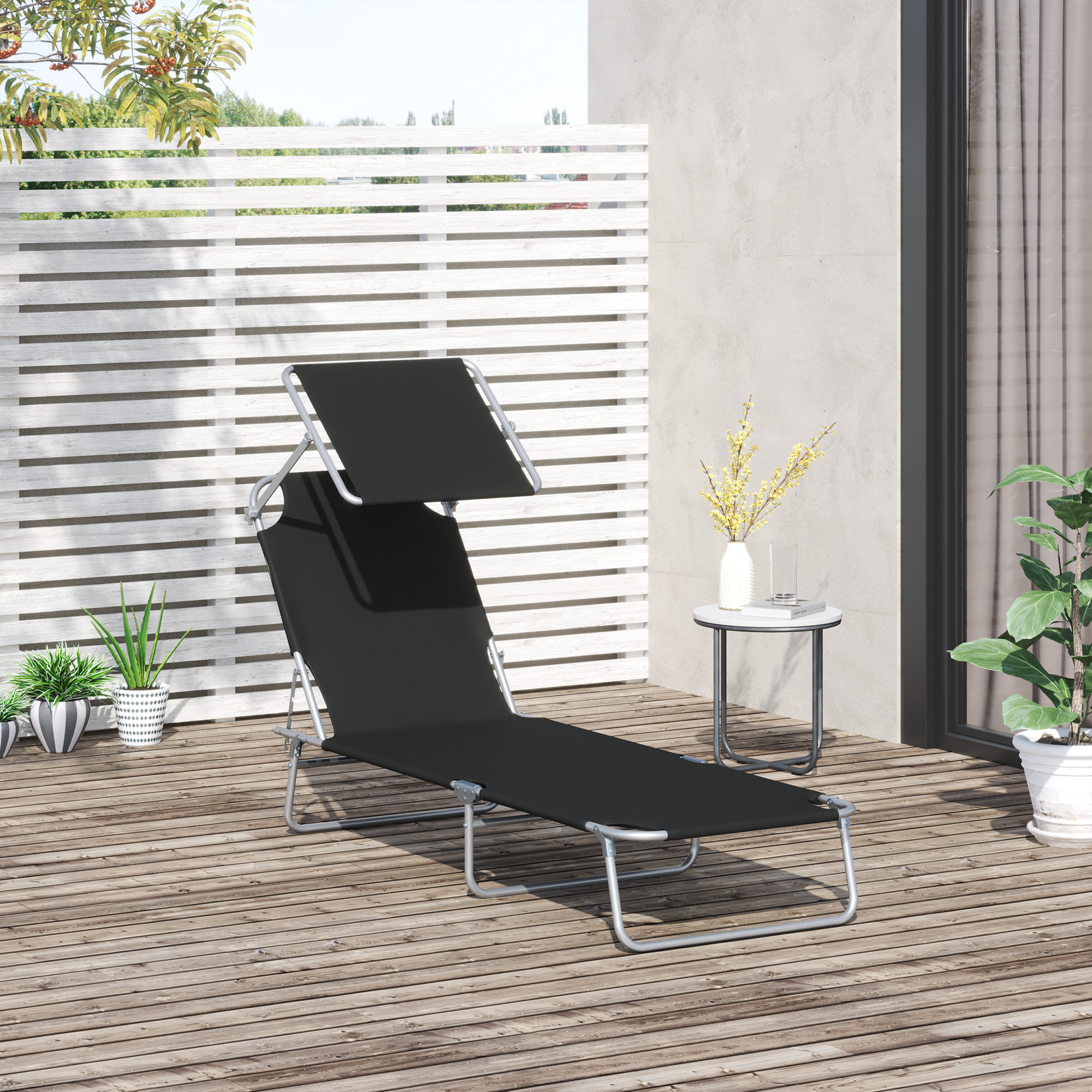 Tumbona negra con dosel en tarima de madera, cerca de plantas y mesa pequeña.