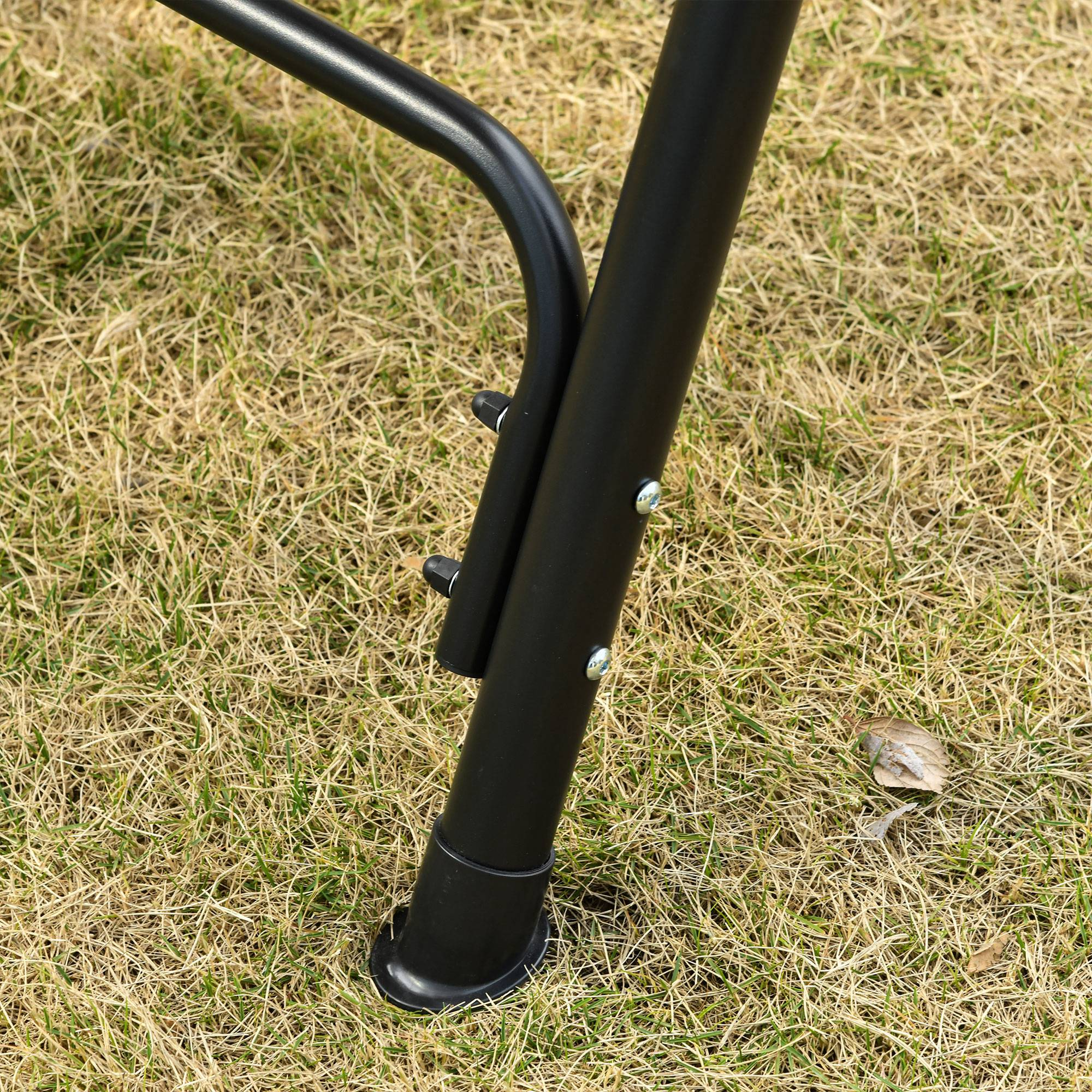 Pata de silla de metal negro sobre hierba seca con tornillos.
