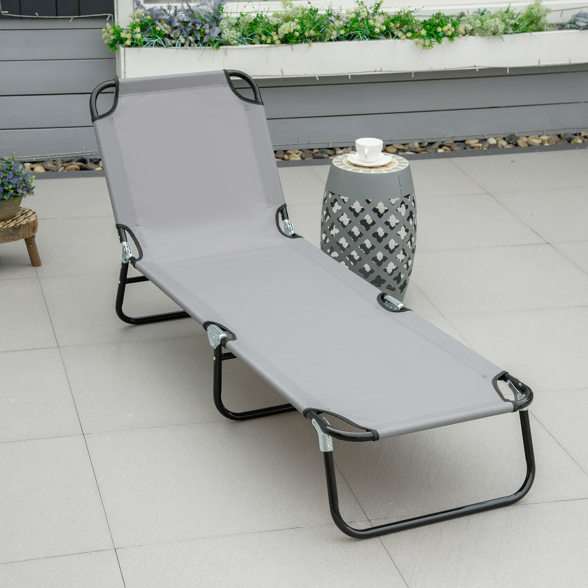 Una sdraio grigia su un patio piastrellato accanto a un tavolino con una tazza.
