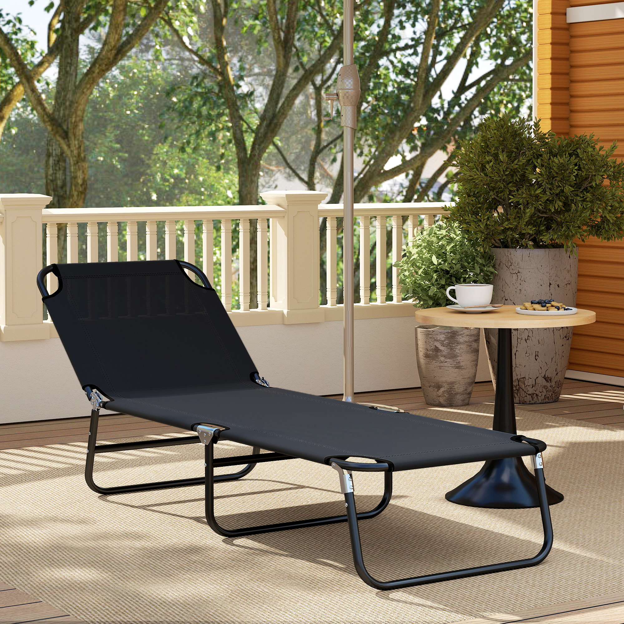 Tumbona negra en terraza de madera con plantas y mesa auxiliar.