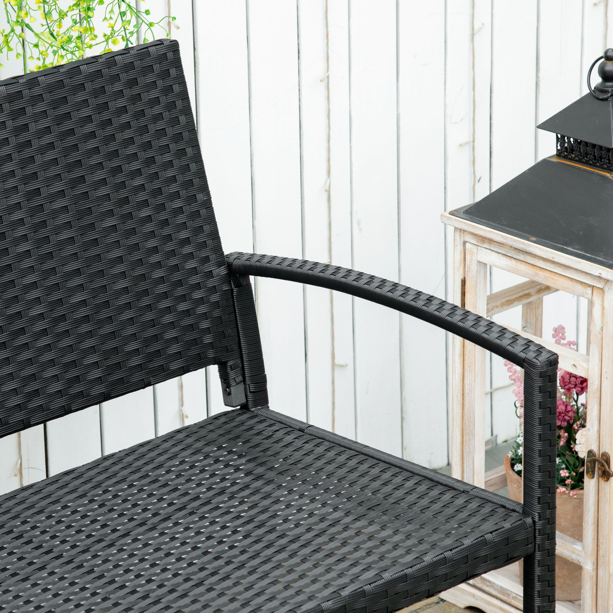 Silla de ratán negra junto a pared de madera blanca con farol y flores.