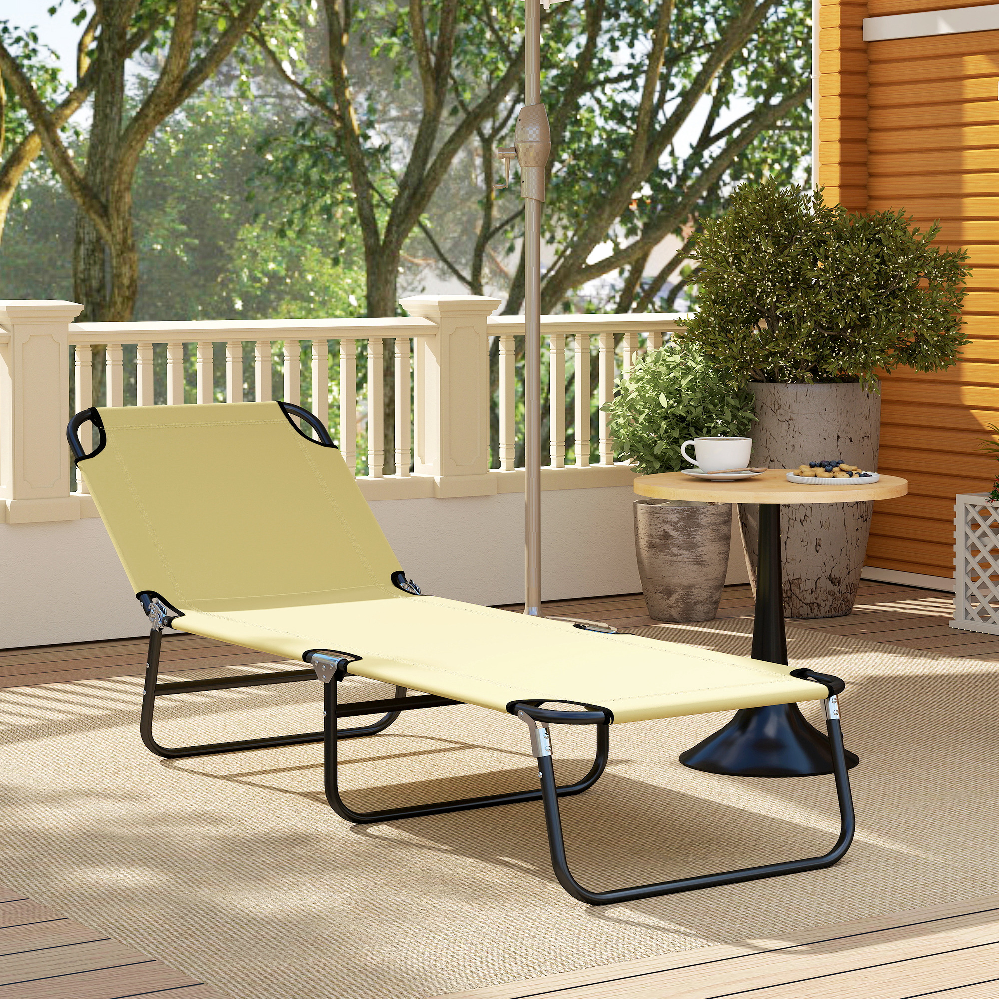 Una tumbona beige se sienta en una terraza de madera junto a una mesa pequeña con una taza y bocadillos.