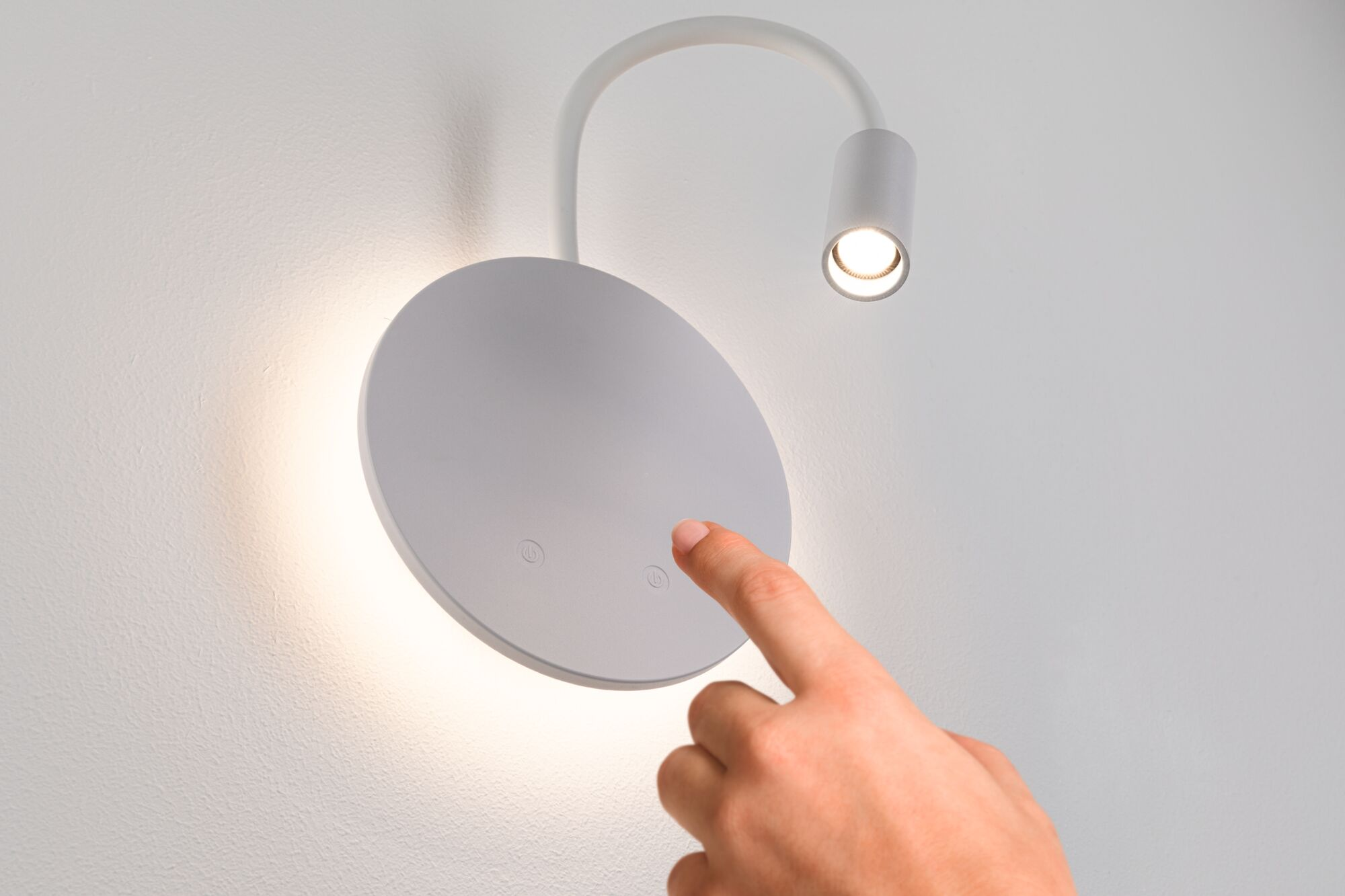 Dłoń dotyka białej lampy ściennej z okrągłym kloszem.