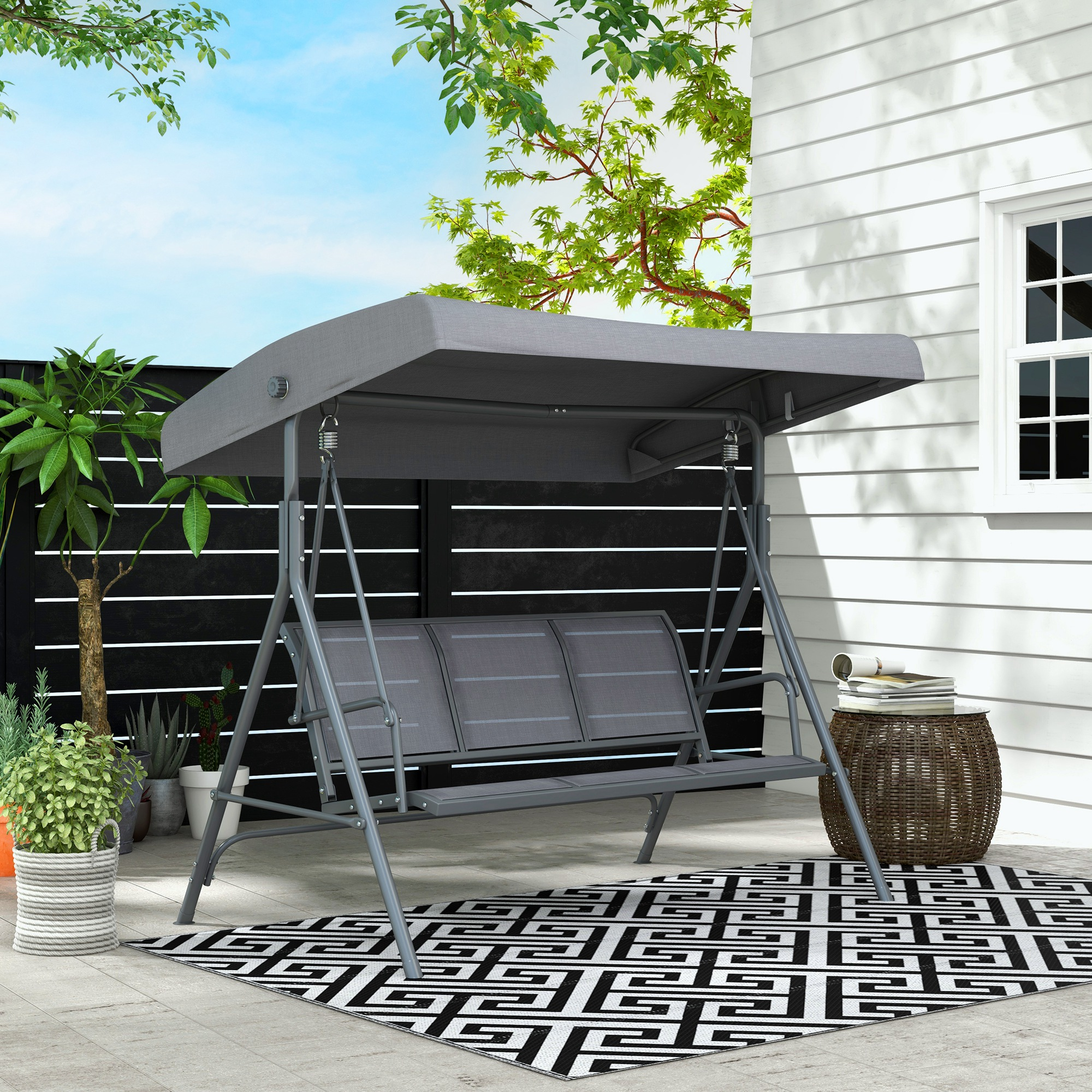Columpio gris en patio con valla negra y casa blanca.