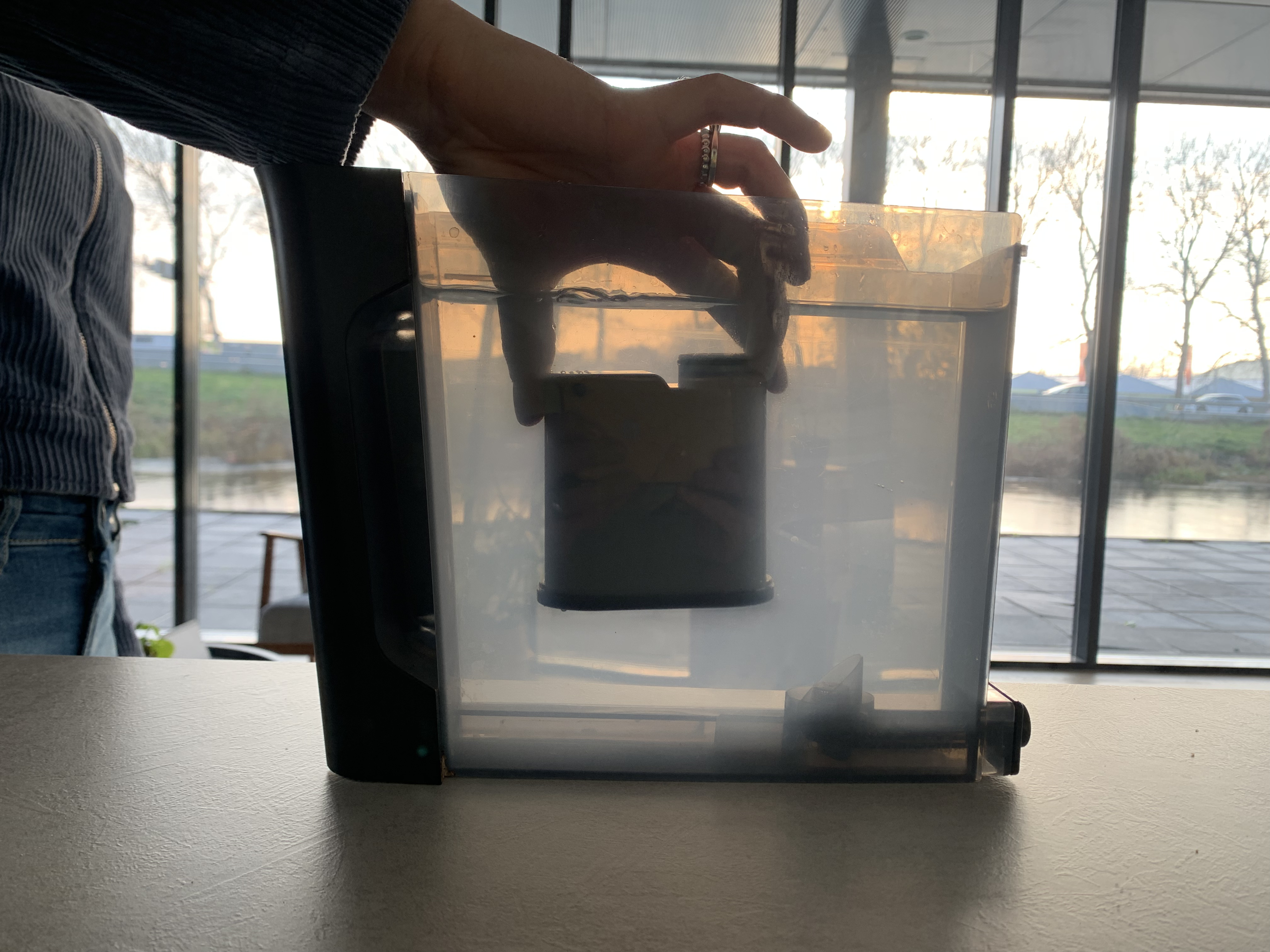 Een hand plaatst een filter in een waterkan. Het is buiten helder.