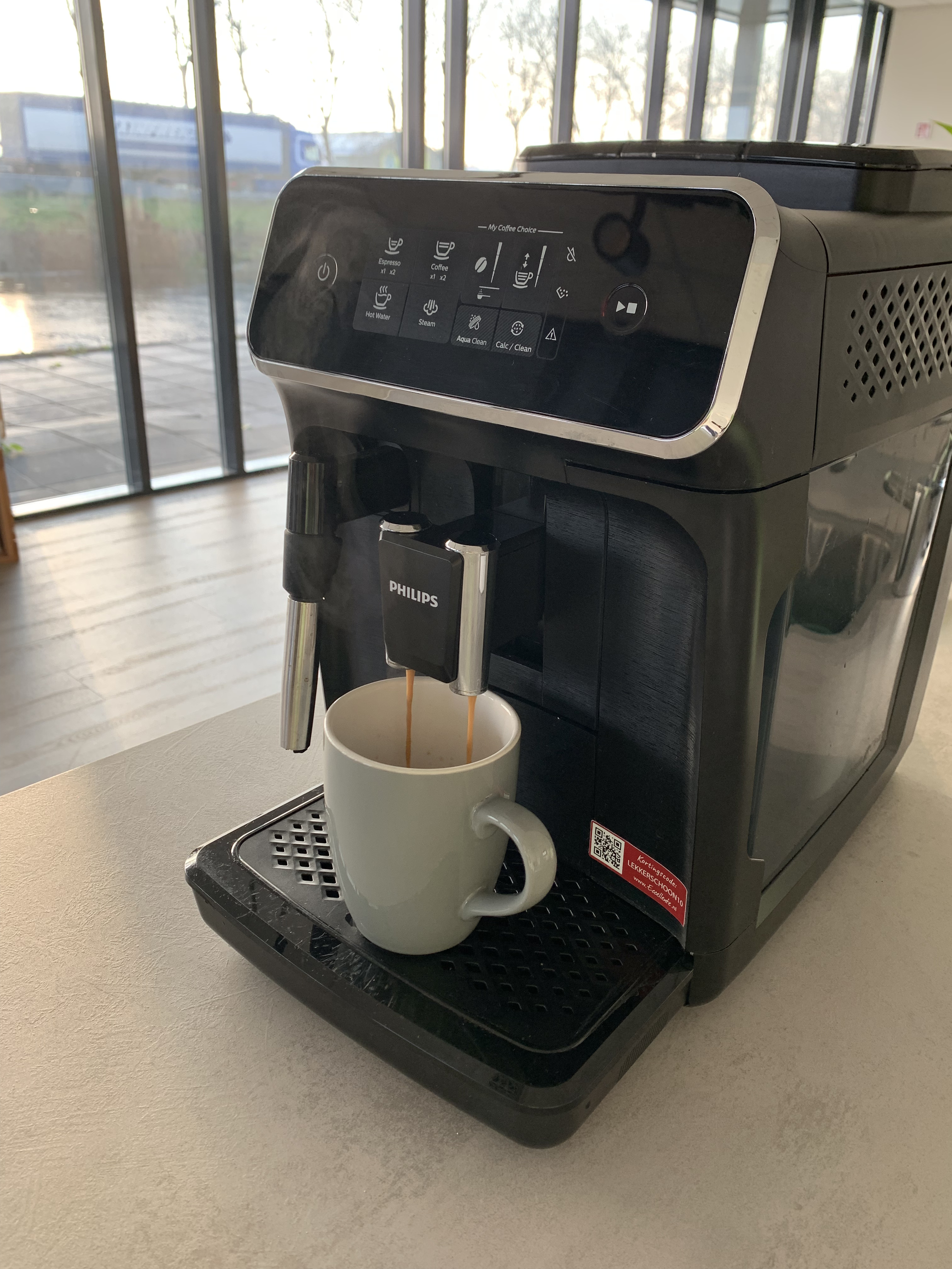 Een koffiezetapparaat zet koffie in een lichtgrijze mok.