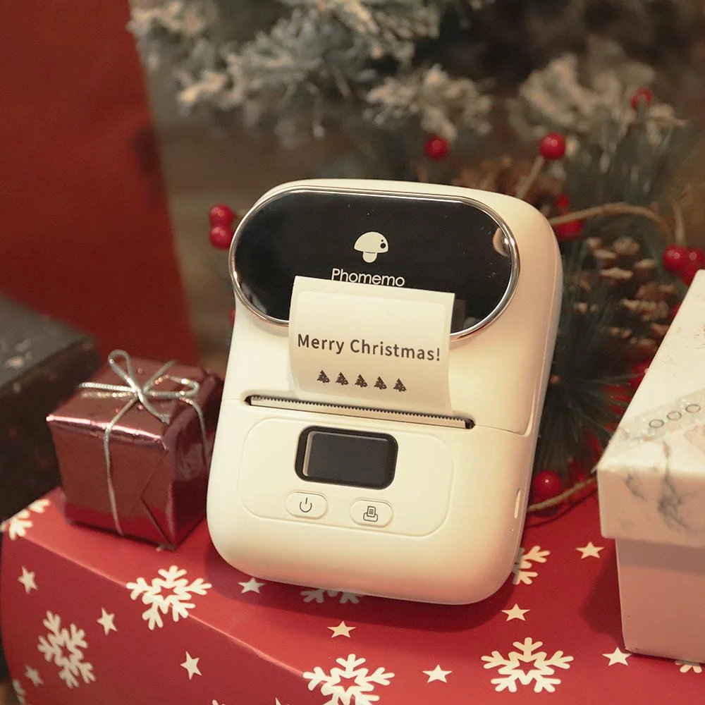 Una stampante Phomemo bianca stampa "Buon Natale!" su un'etichetta, circondata da regali natalizi.