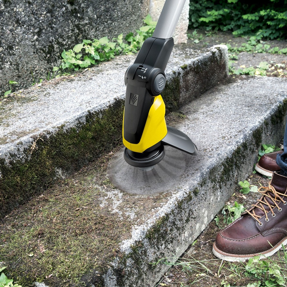 Ein gelber und schwarzer Reiniger säubert eine bemooste Steintreppe. Braunen Schuhen.