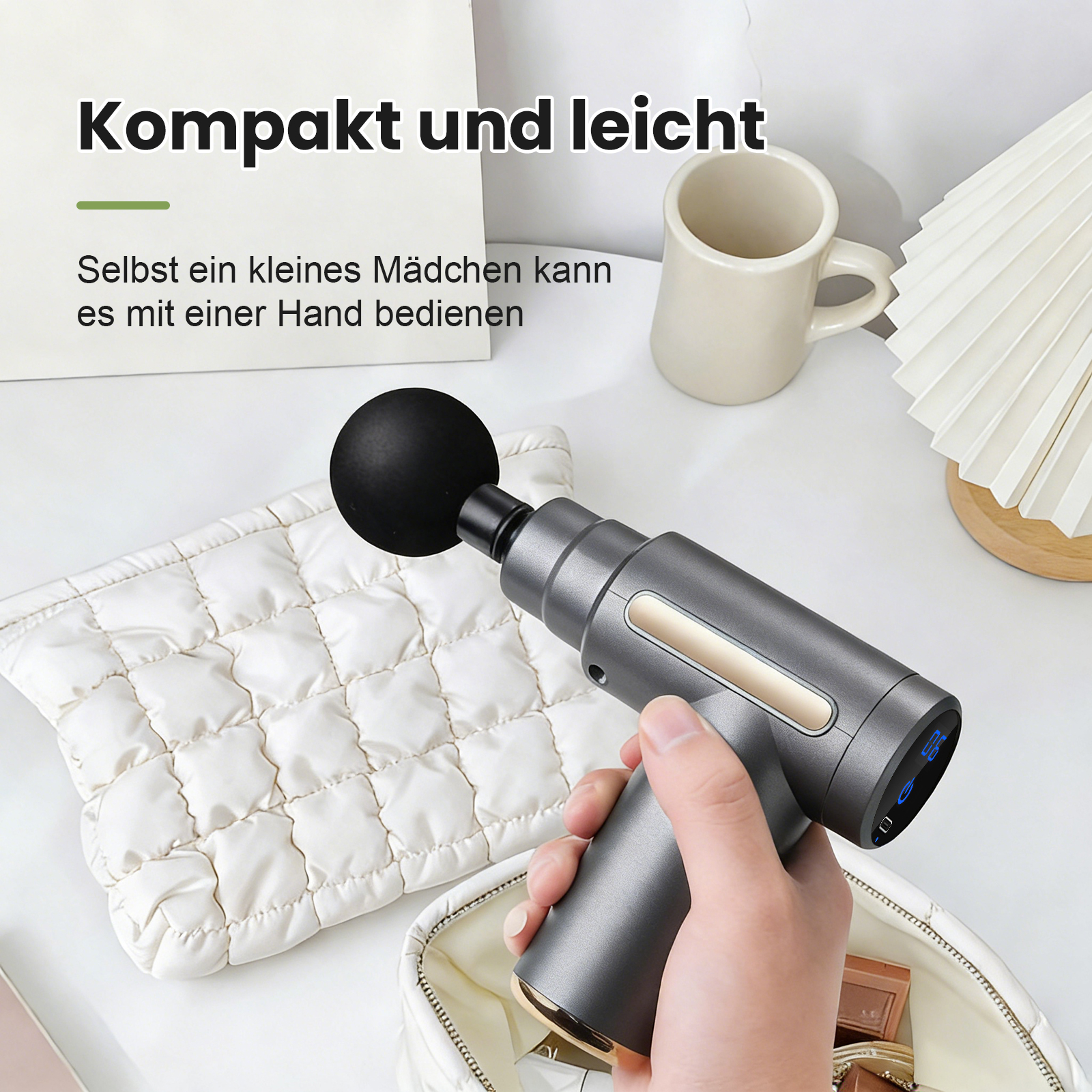Graue Massagepistole mit schwarzem Ballaufsatz neben weißer Tasche.