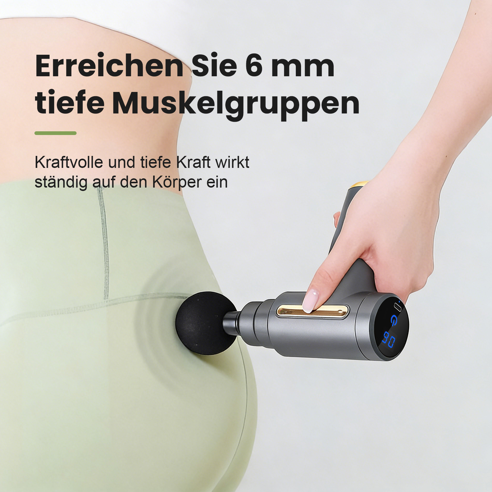 Hand hält Massagepistole an Hüfte/Oberschenkel. Graue Pistole mit digitaler Anzeige.
