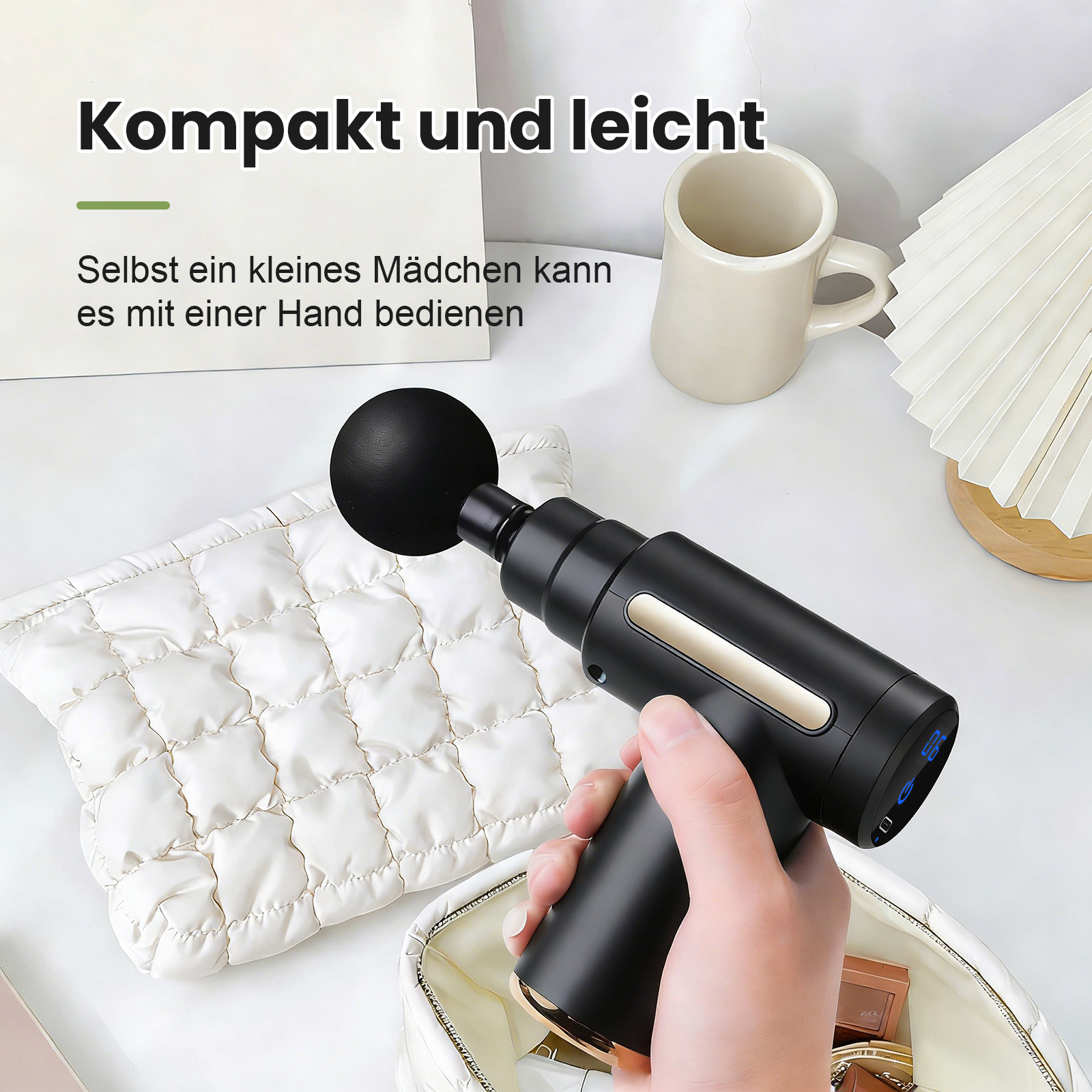 Hand hält schwarzes Massagegerät neben gepolsterter Tasche. Becher und Lampe im Hintergrund.