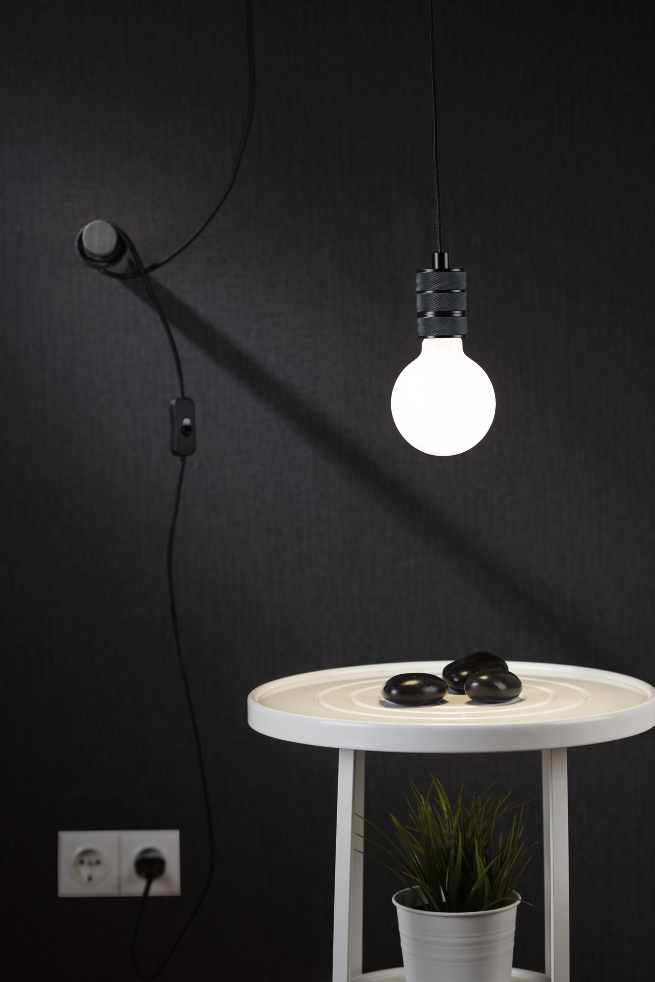 Eine weiße Nachttischlampe mit schwarzen Steinen und einer Pflanze.