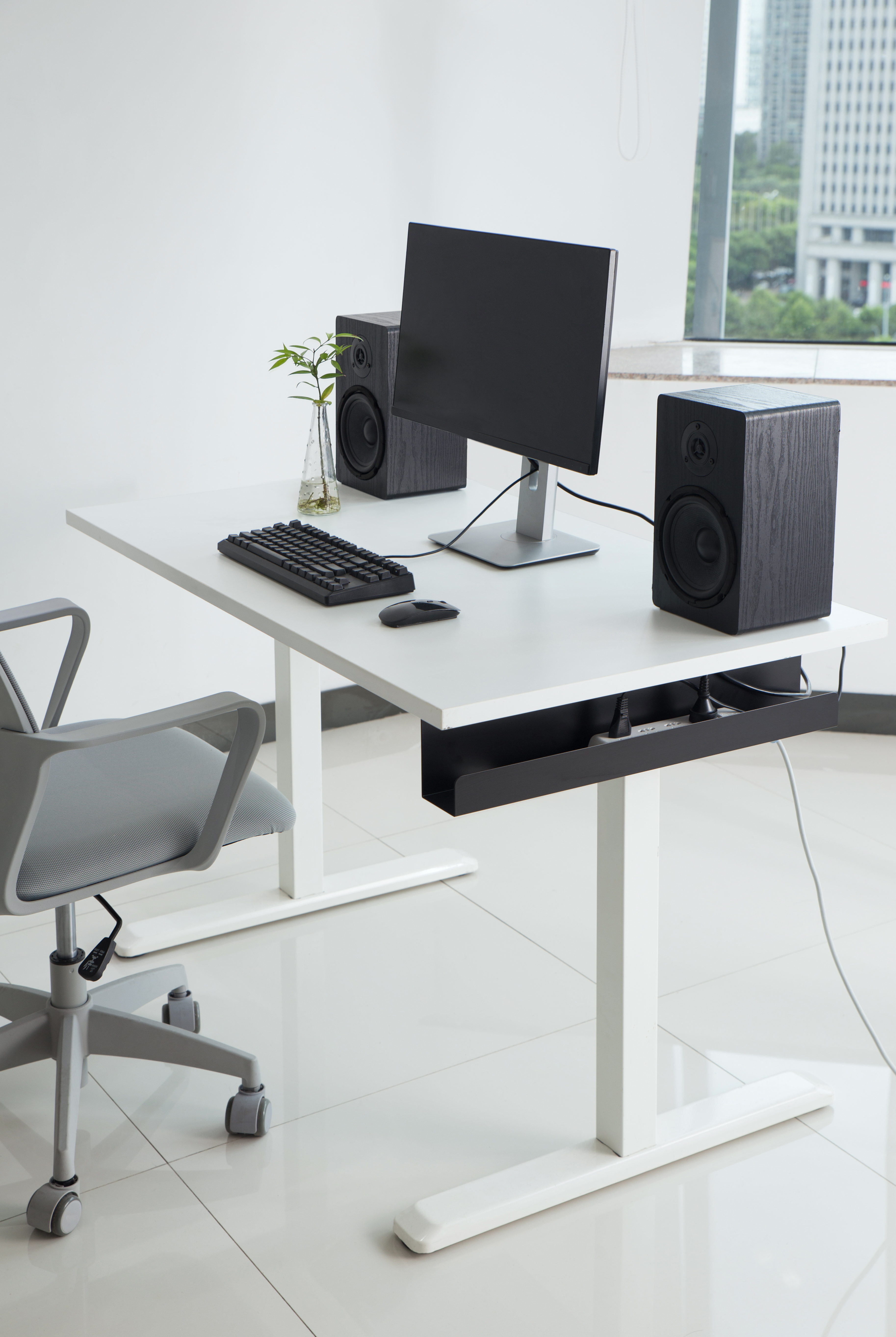 Un escritorio blanco con monitor, teclado, ratón, altavoces y silla.