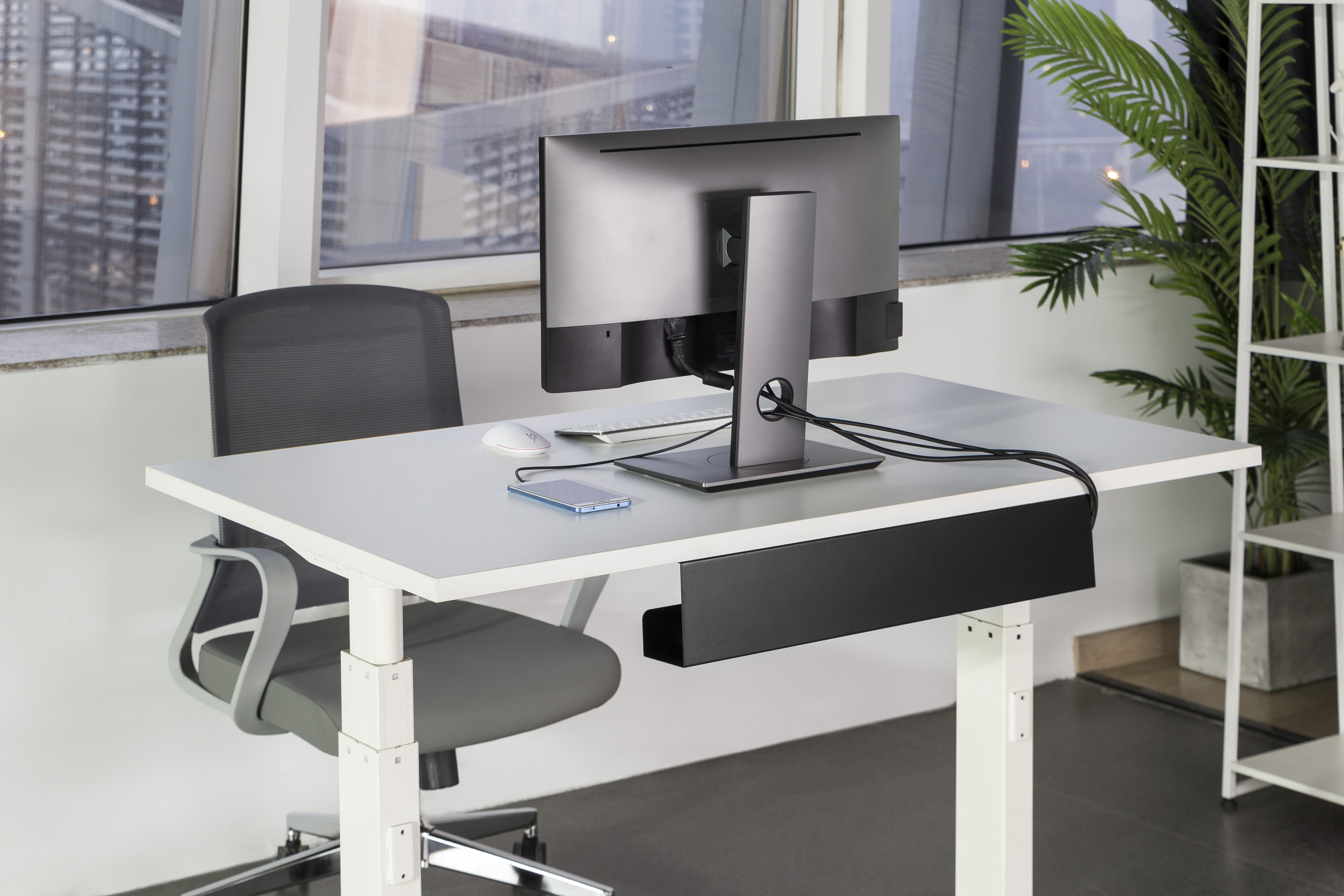 Un escritorio con monitor, teclado, ratón y teléfono. Una silla de oficina delante.