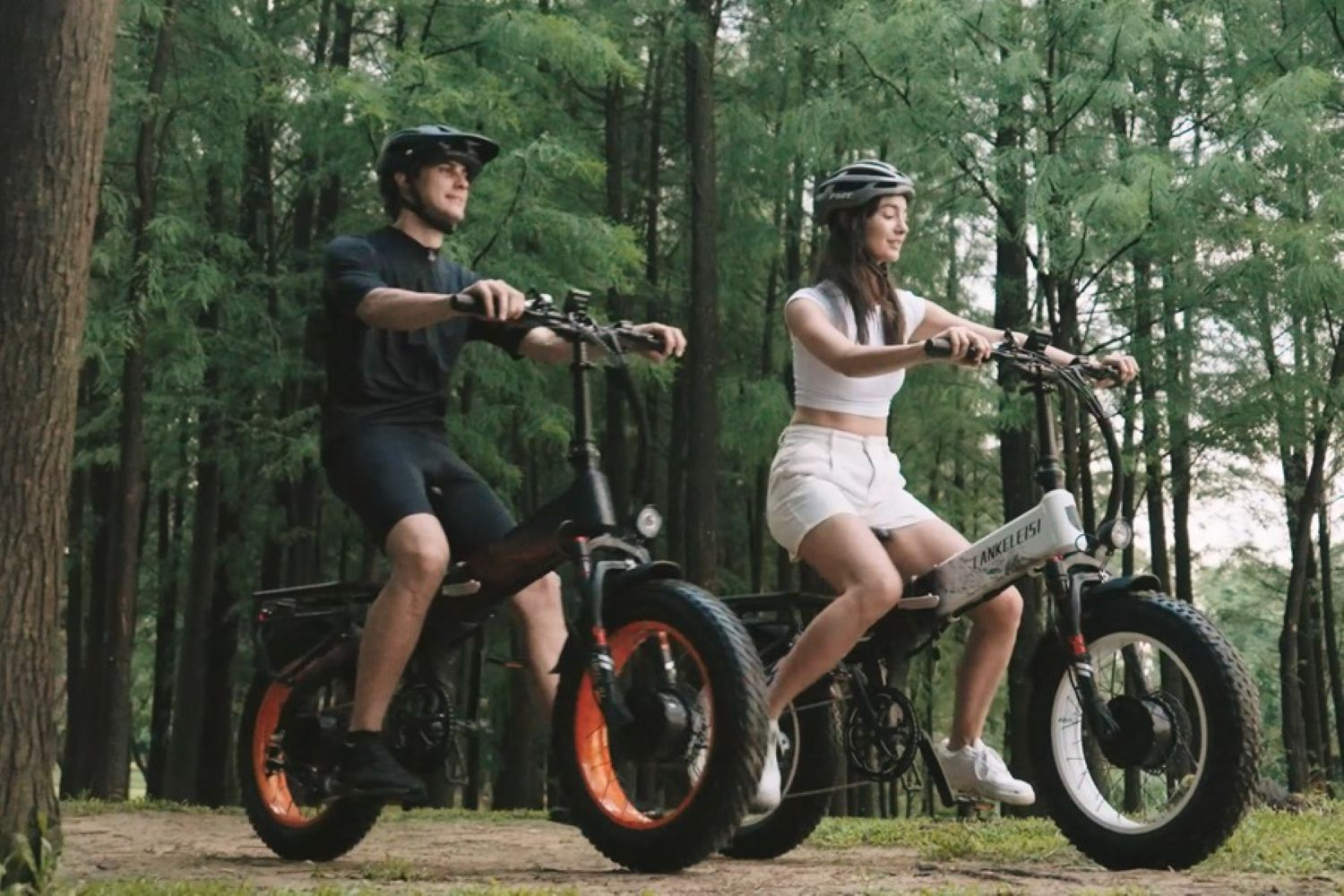 Un uomo e una donna vanno in e-bike in un bosco, entrambi con casco.