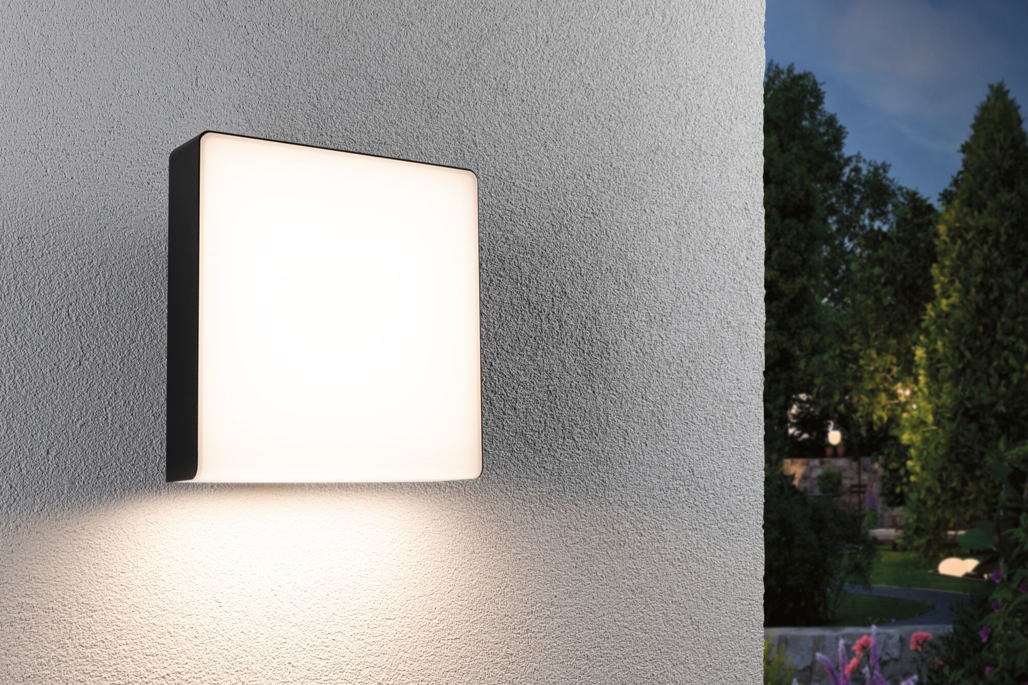 Kwadratowa lampa ścienna oświetla teksturowaną ścianę i ogród nocą.