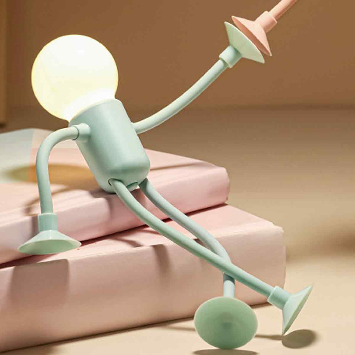 Eine hellgrüne Lampe in Form einer Figur sitzt auf rosa Büchern.