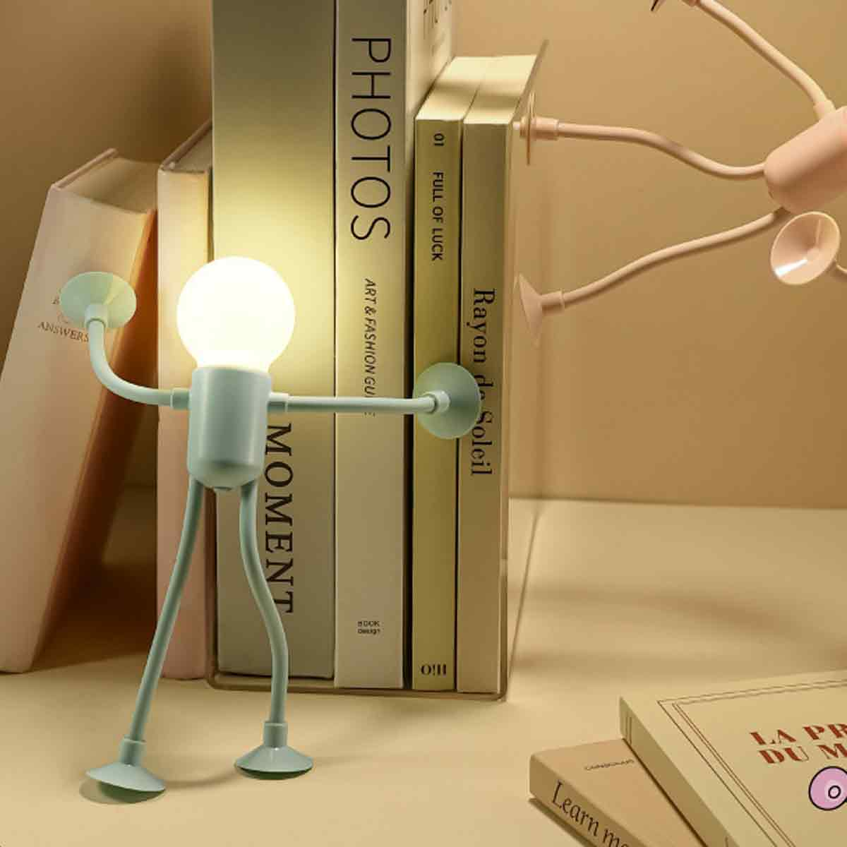 Eine blaue Lampe in Menschenform steht vor Büchern. Heller Lampenschirm oben.