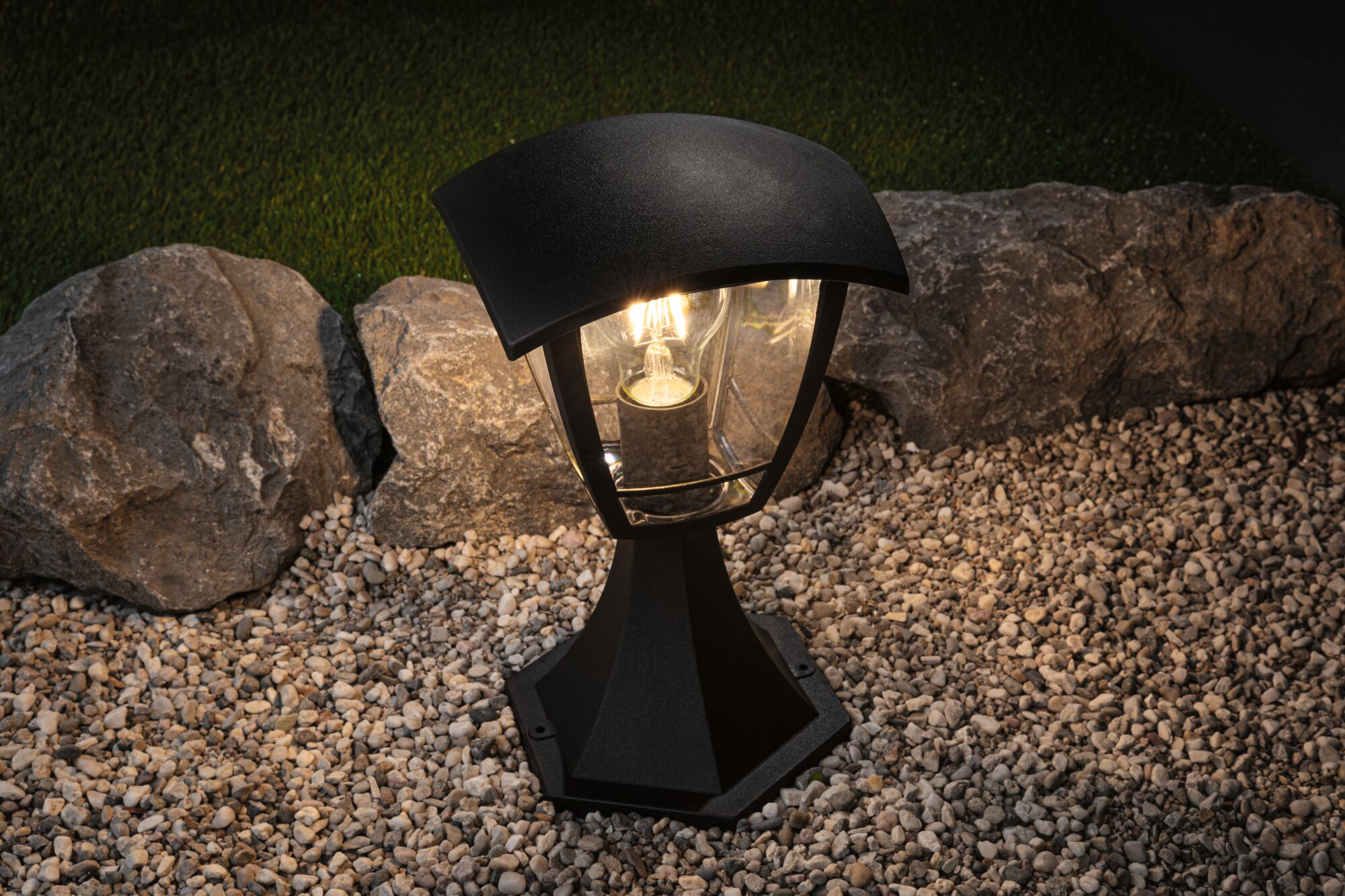 Czarna lampa zewnętrzna na żwirze z kamieniami i trawą.