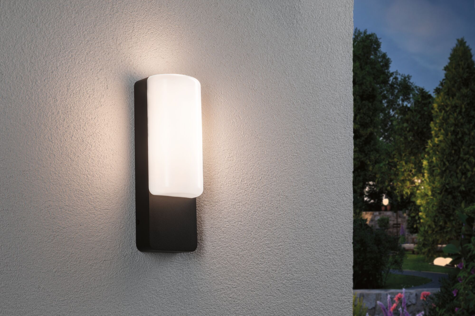 Nowoczesna lampa ścienna oświetla teksturowaną ścianę. Na zewnątrz jest ciemno z drzewami.