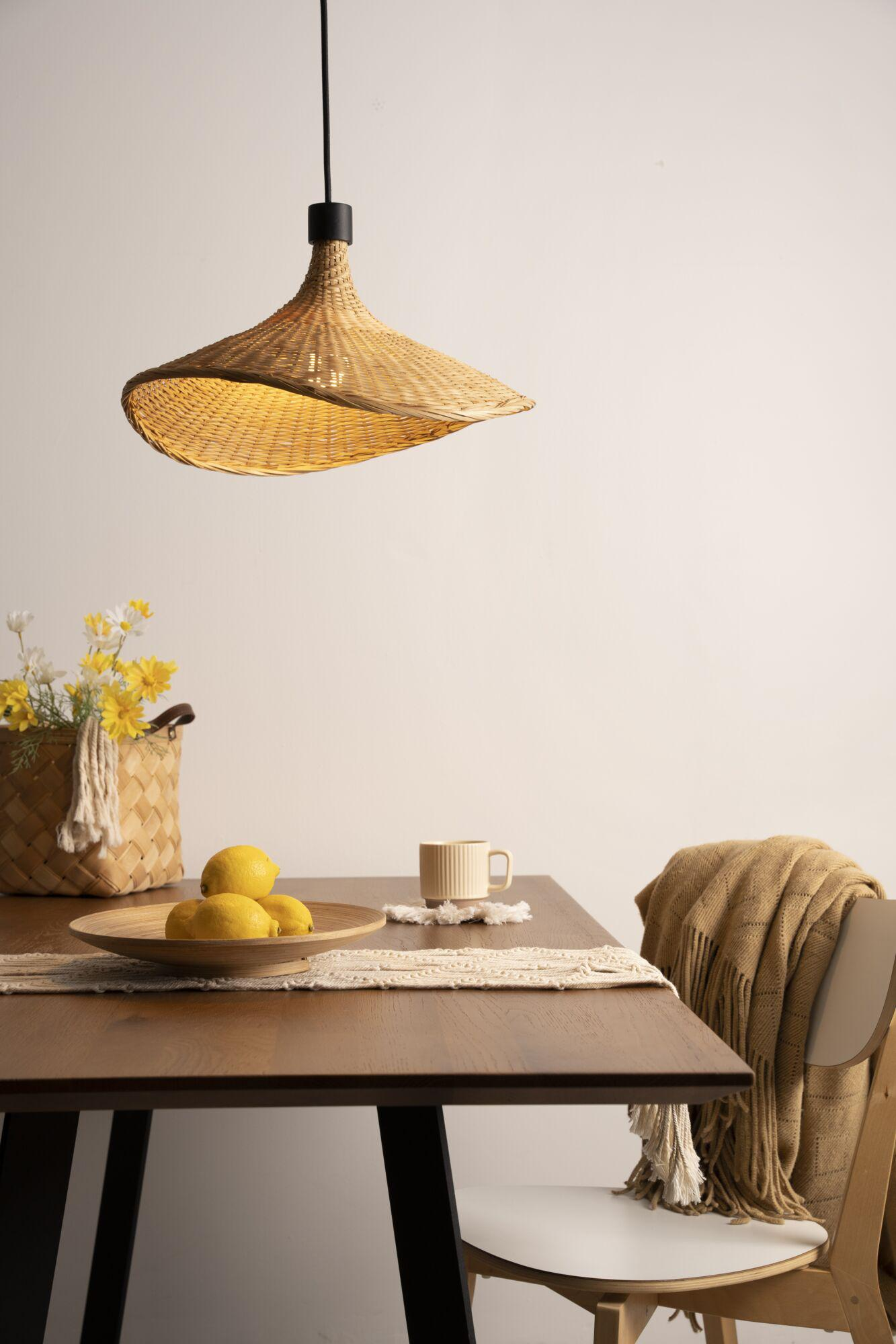 Stół jadalniany z cytrynami, kwiatami i kubkiem pod rattanową lampą.