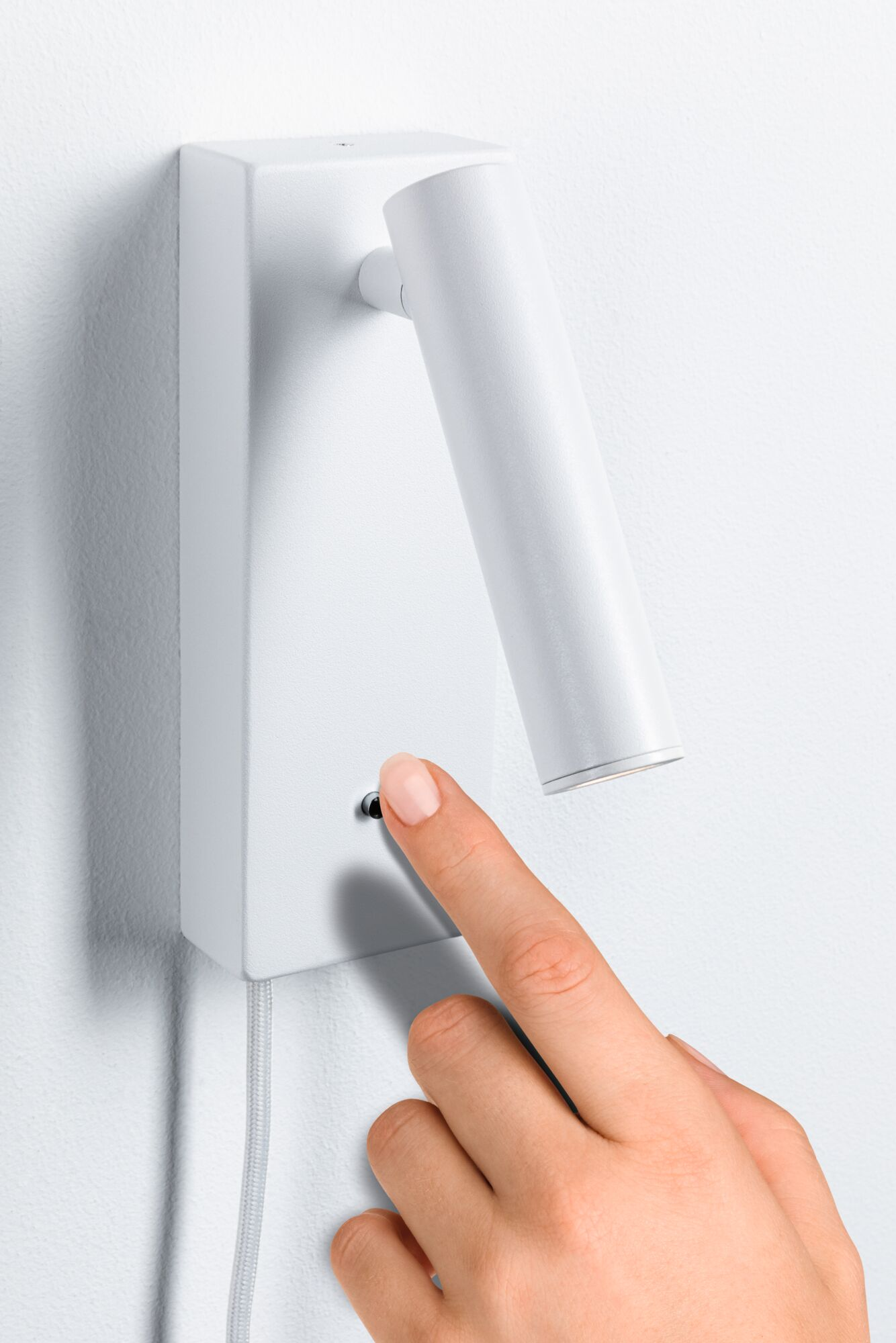 Dłoń włącza przełącznik białej lampy ściennej.