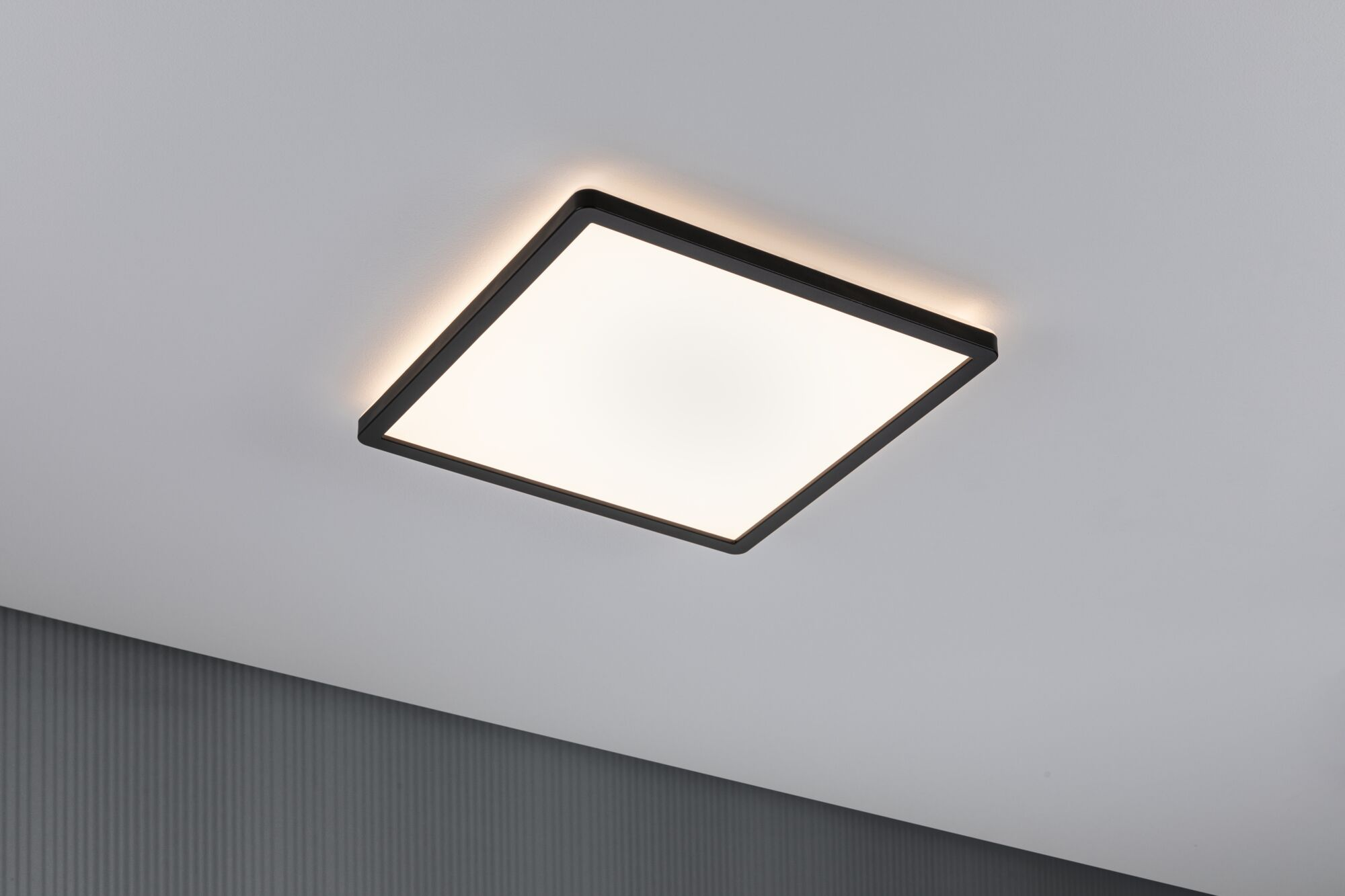 Una lampada da soffitto quadrata con cornice nera, che emette luce diffusa su un soffitto bianco.