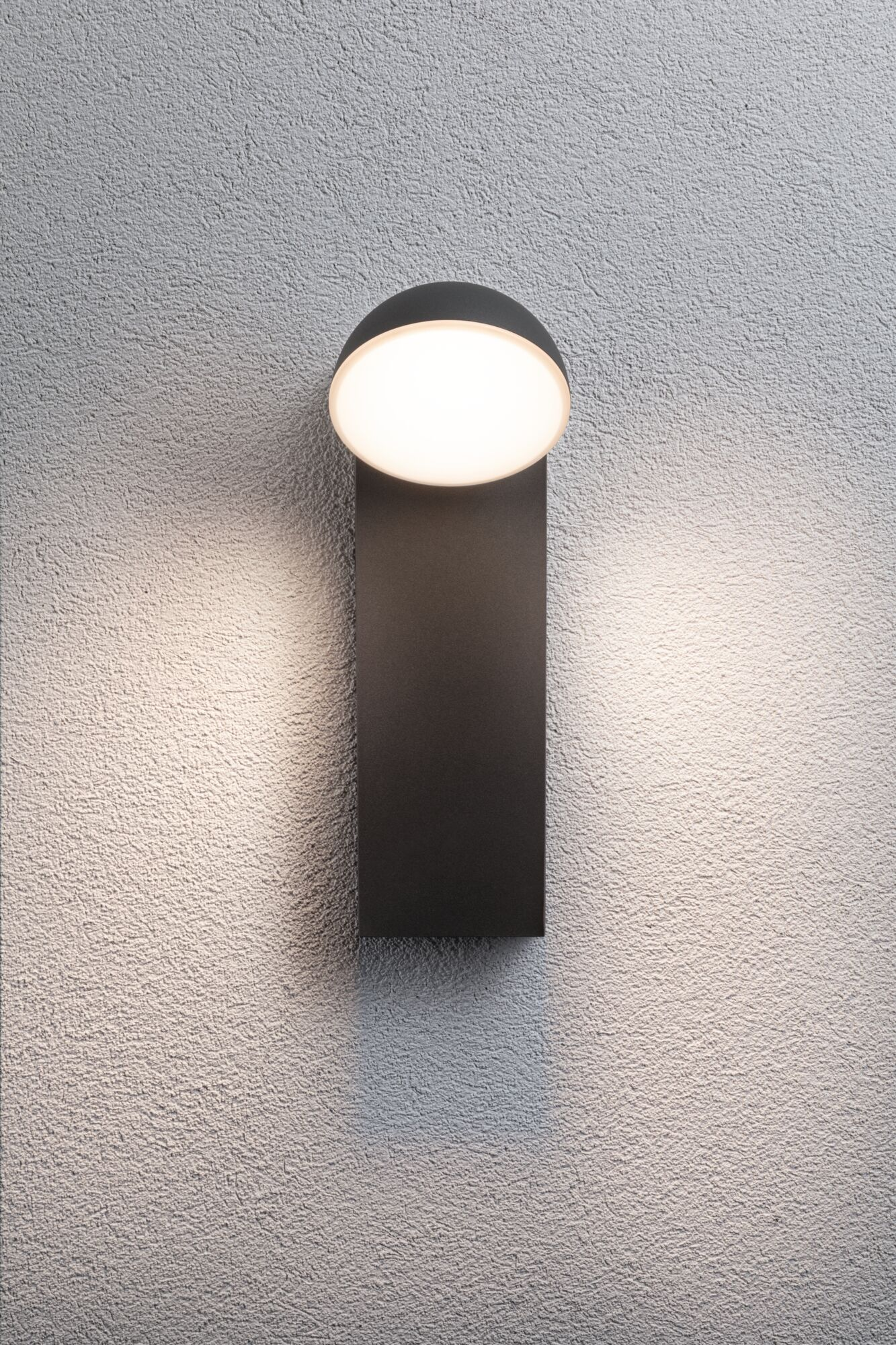 Eine dunkle Wandlampe mit einem runden Licht, das an einer strukturierten Wand leuchtet.