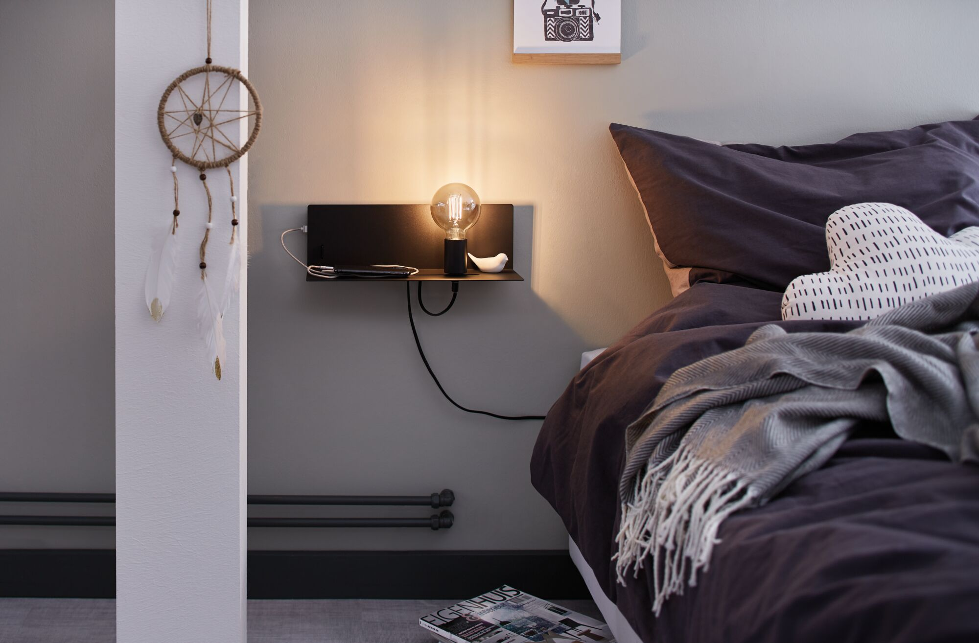 Szafka nocna z lampą, telefonem i ptaszkiem. Po lewej wisi łapacz snów.