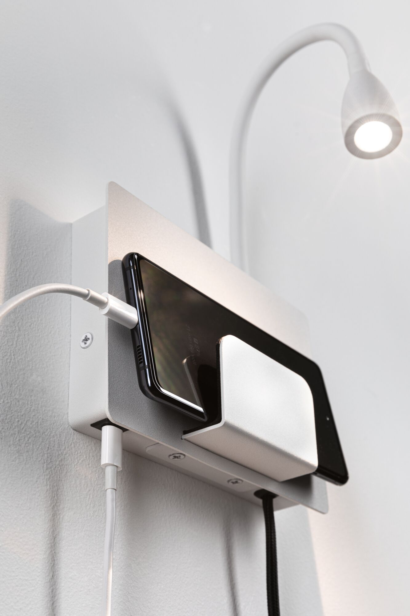 Smartfon i tablet ładują się na uchwycie ściennym z lampką.