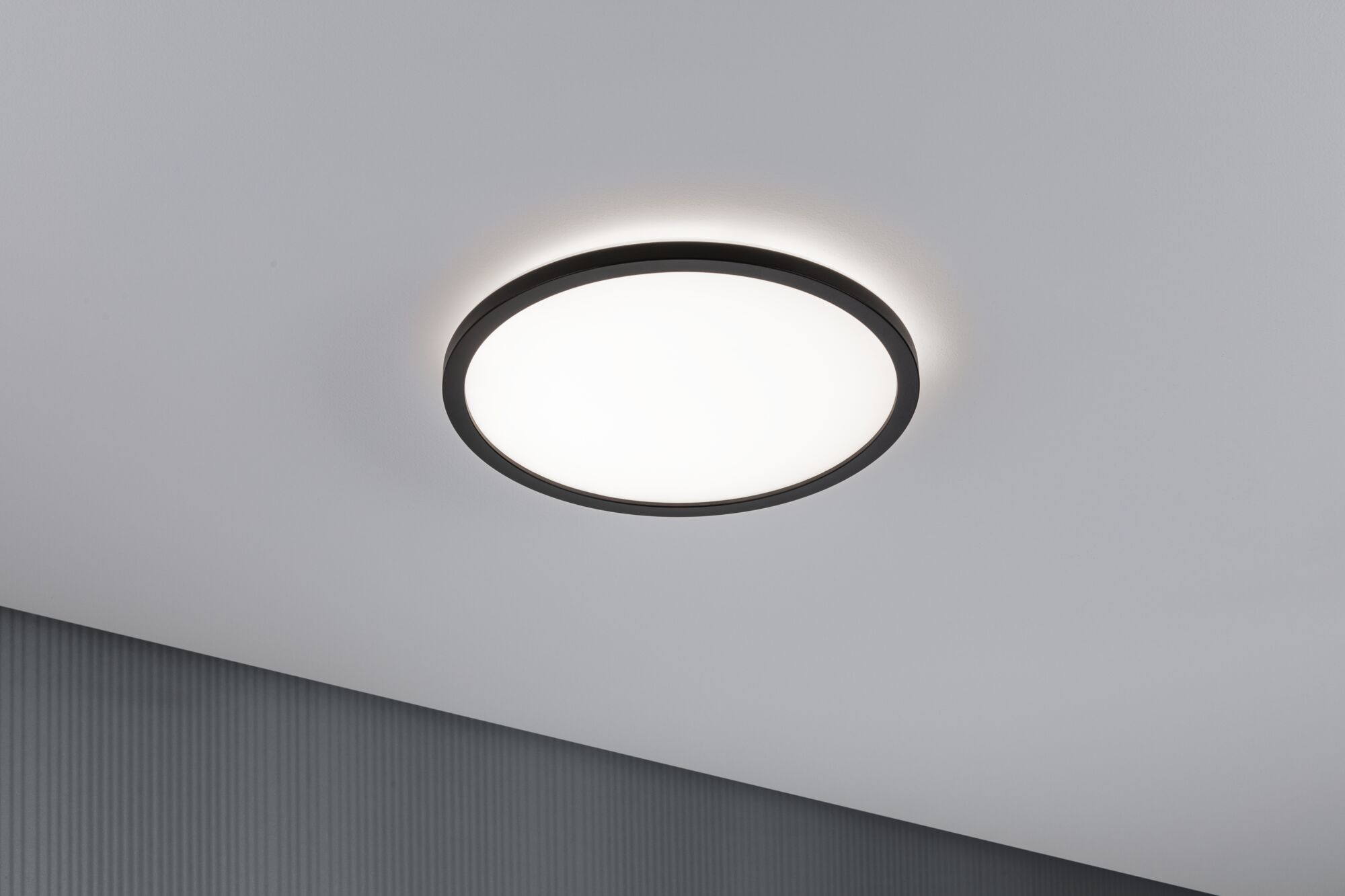 Una plafoniera rotonda con bordo nero brilla su un soffitto bianco.