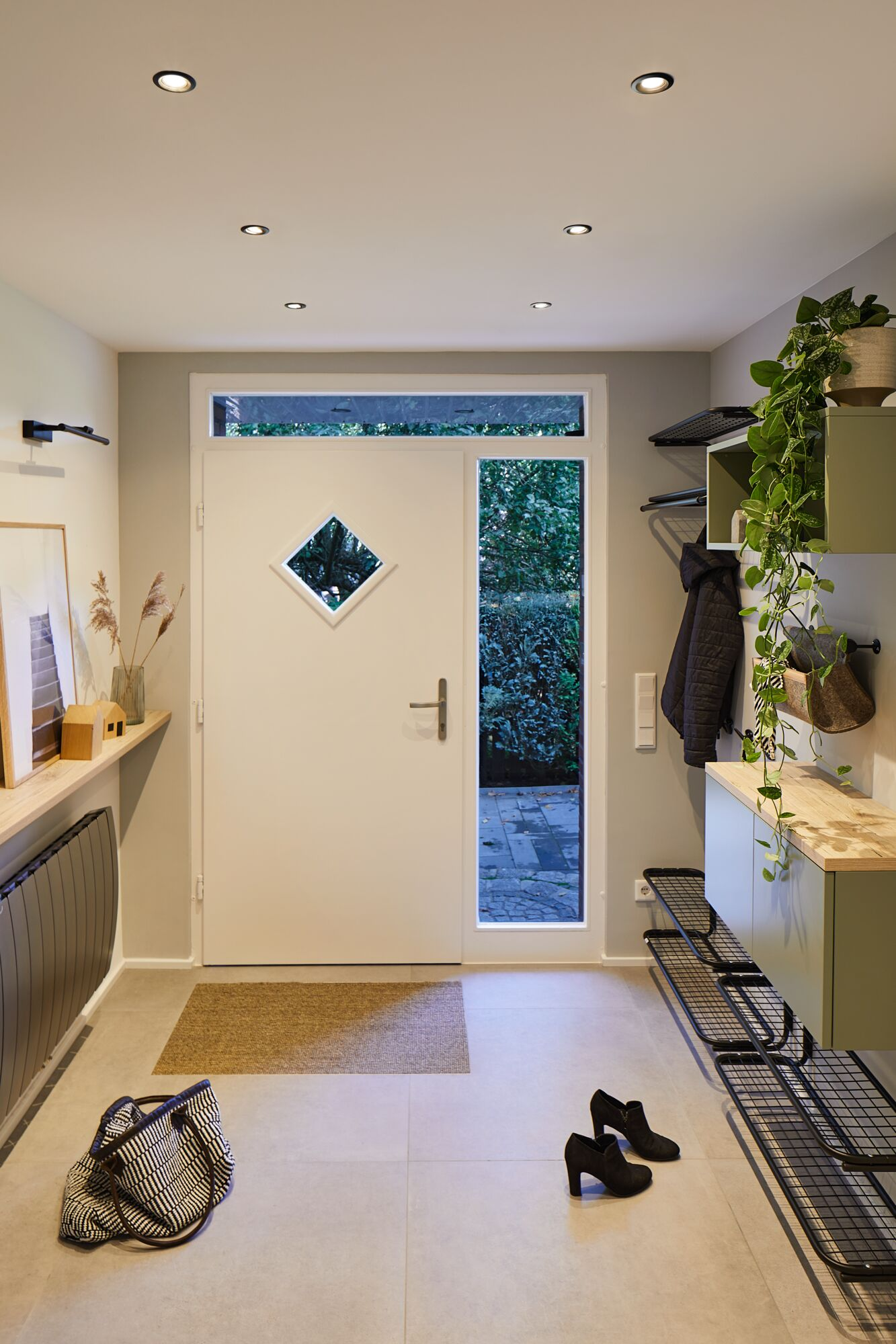 Jasny przedpokój z białymi drzwiami, roślinami i butami.