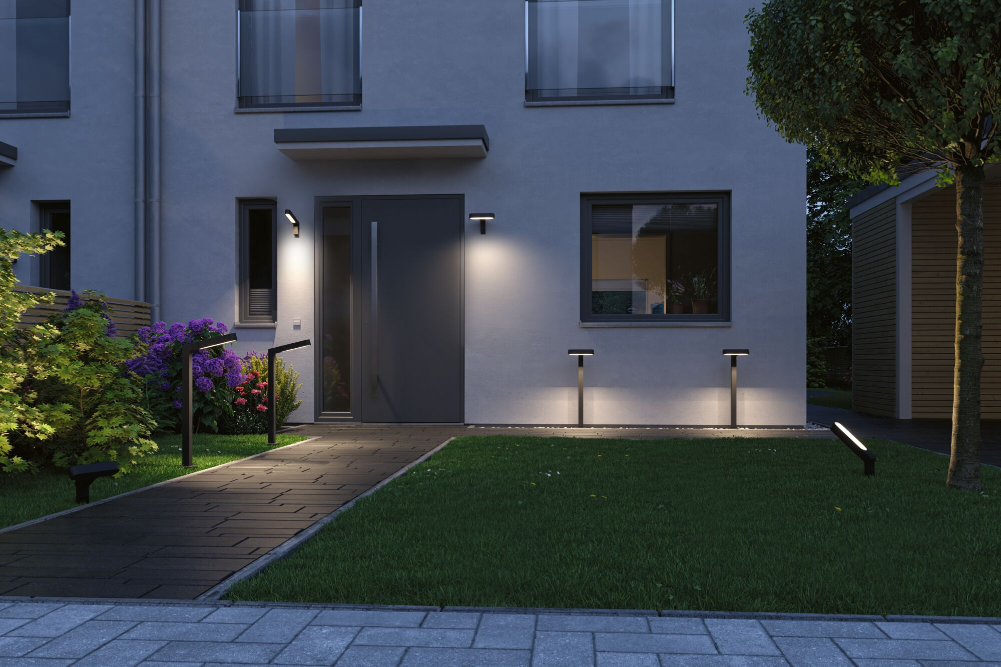 Ein Weg beleuchtet ein modernes Haus mit einem dunklen Tor, grüner Rasen und lila Blumen.